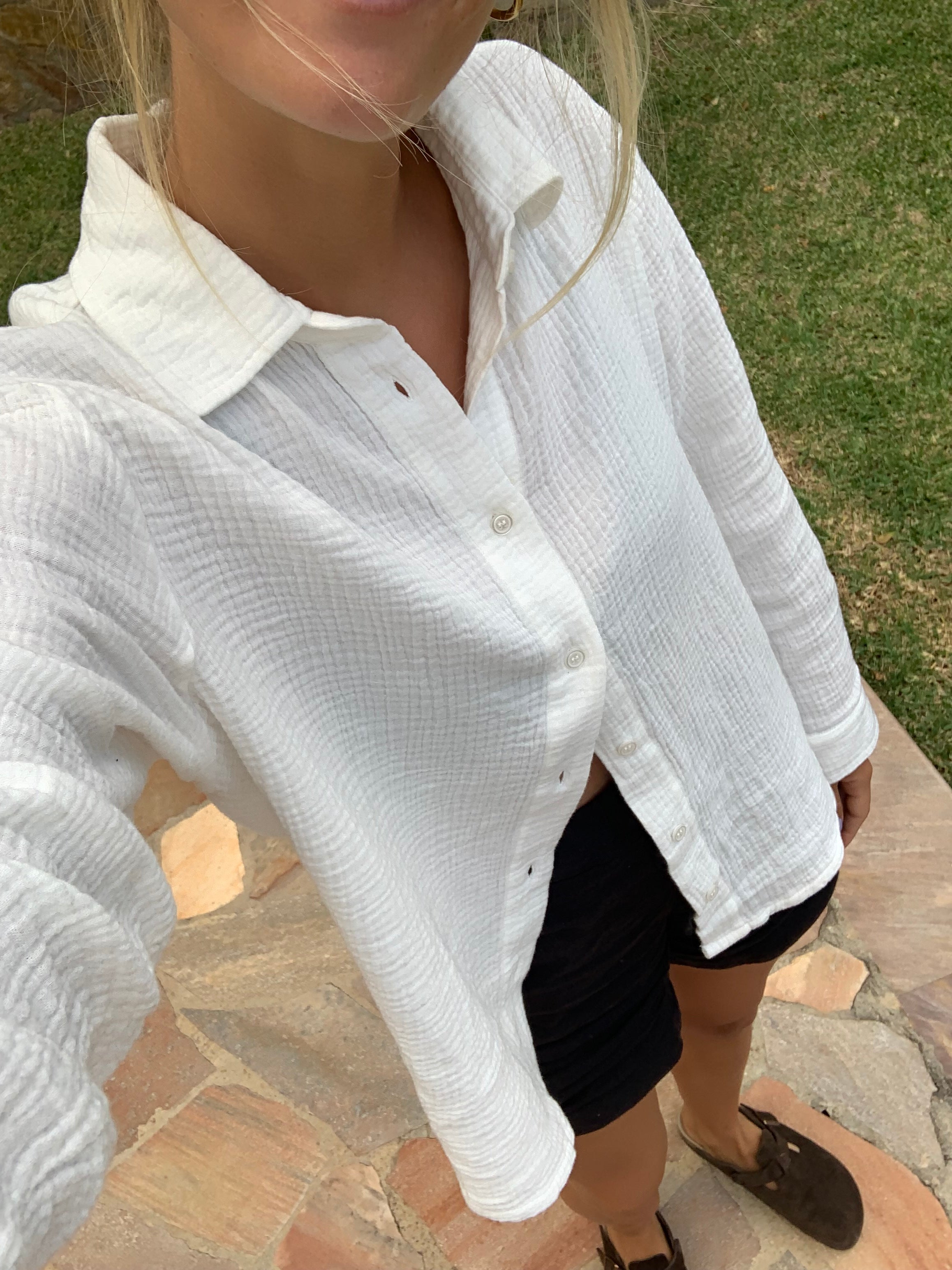 Frau trägt cremeweiße Fair-Fashion-Musselinbluse von FUXBAU mit schwarzer Leinenshorts.