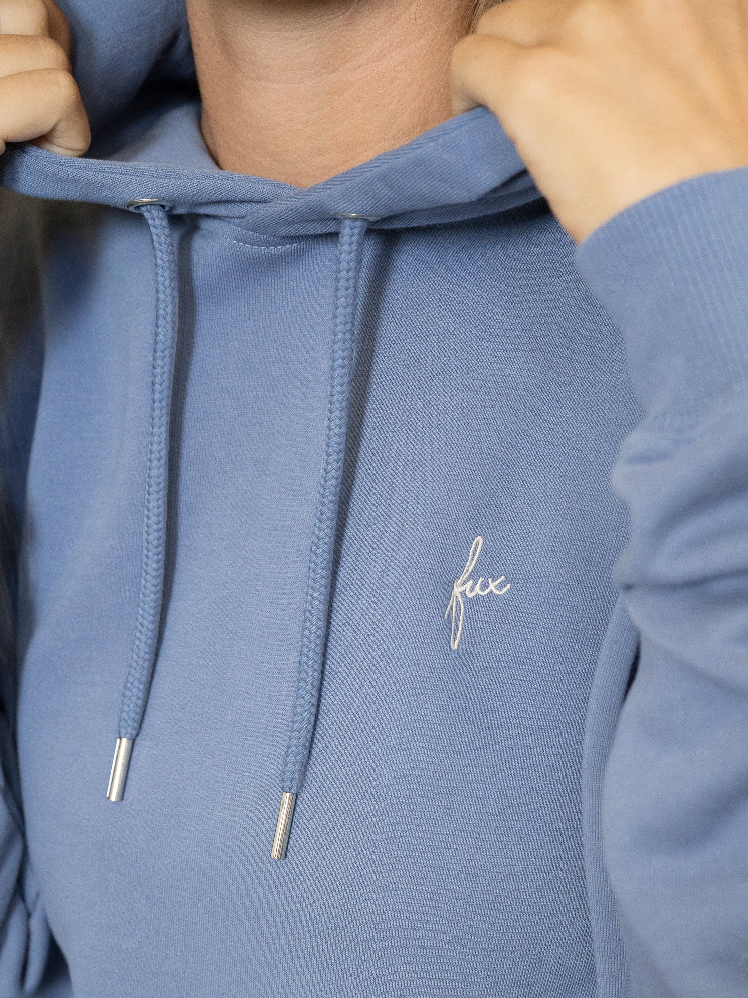 Detailansicht des Brustbereichs mit gesticktem „fux“-Logo und Kordelzug der Kapuze.