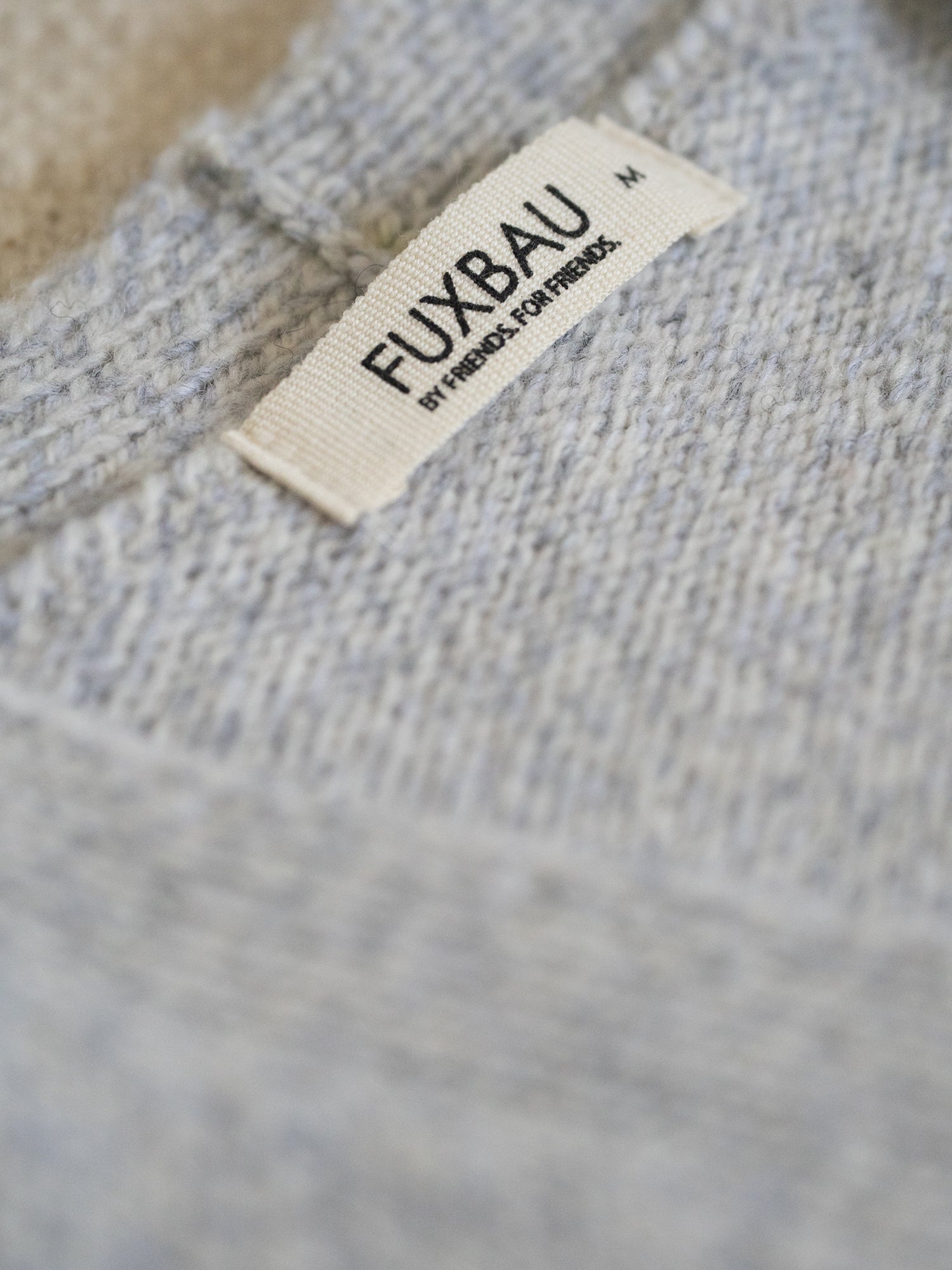 Nahaufnahme des FUXBAU Labels auf der graumelierten Merino Strickweste – gefertigt in Deutschland aus 100 % Merinowolle