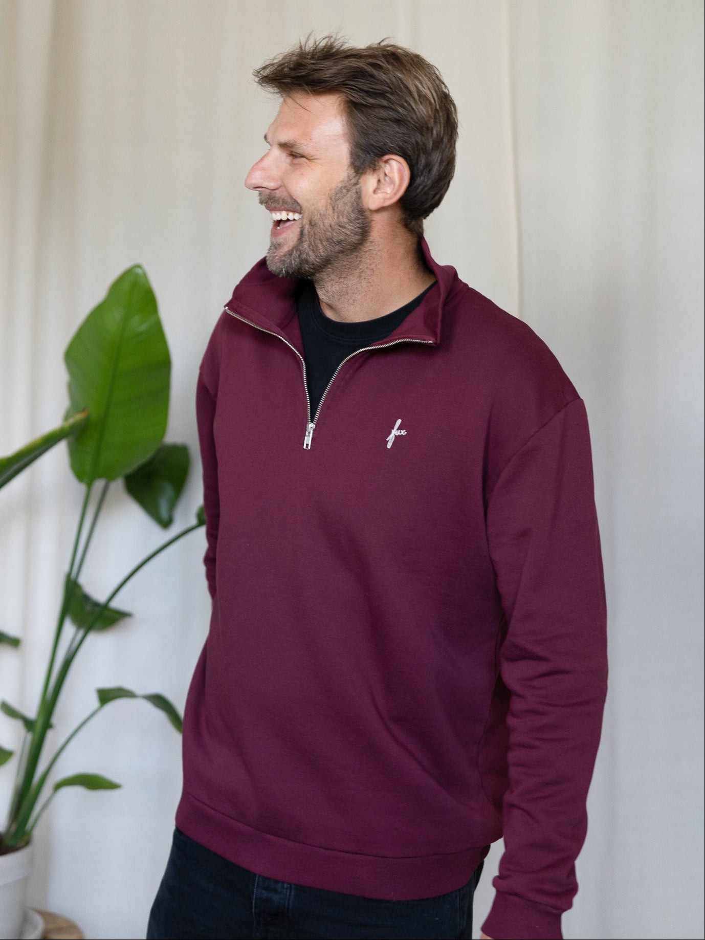 Seitliche Ansicht Mann mit FUXBAU Half-Zip Sweater in Bordeaux – nachhaltiger Herrenpullover aus Biobaumwolle.