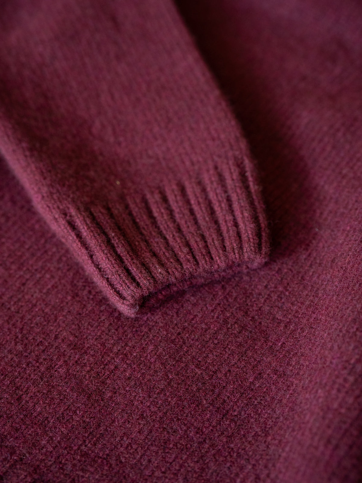 Detailaufnahme eines bordeauxfarbenen Merino Strickpullovers mit geripptem Ärmelbündchen