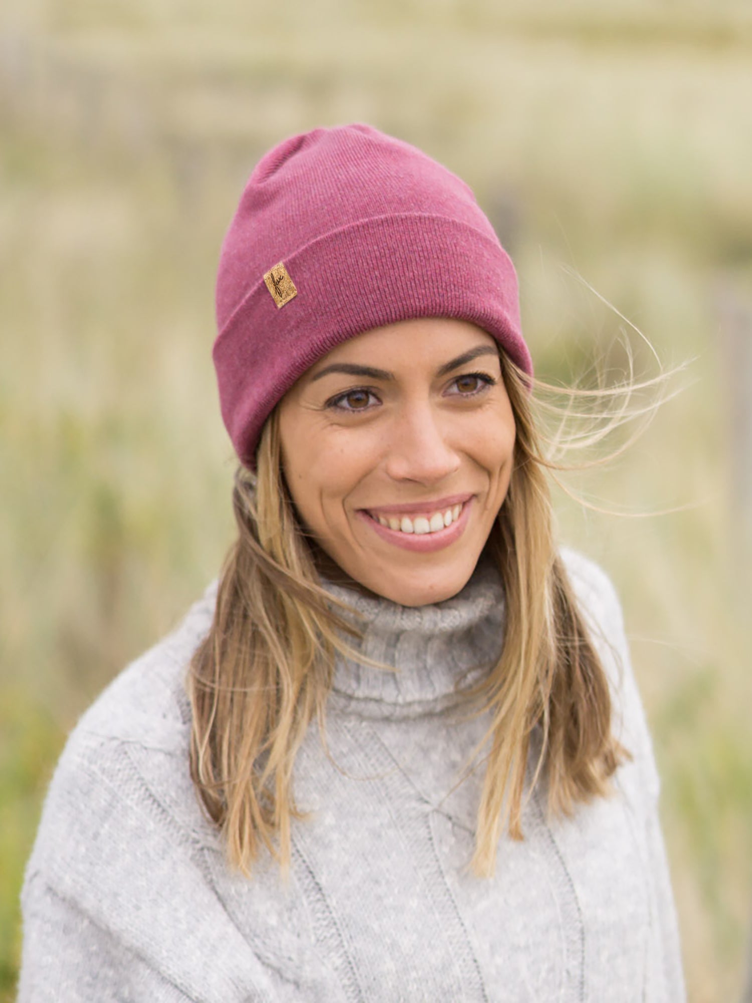 Merino-Kork Beanie Himbeere – nachhaltige Mütze aus Merinowolle, fair in Deutschland hergestellt, Modell lächelt im grauen Strickpullover