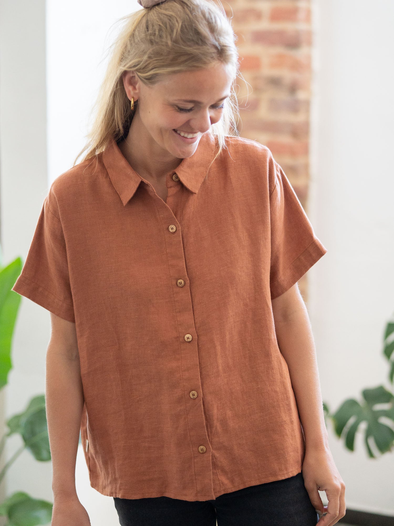 Eine junge, blonde Frau trägt eine nachhaltige Fair Fashion Kurzarm Leinenbluse in rotbraun von FUXBAU.