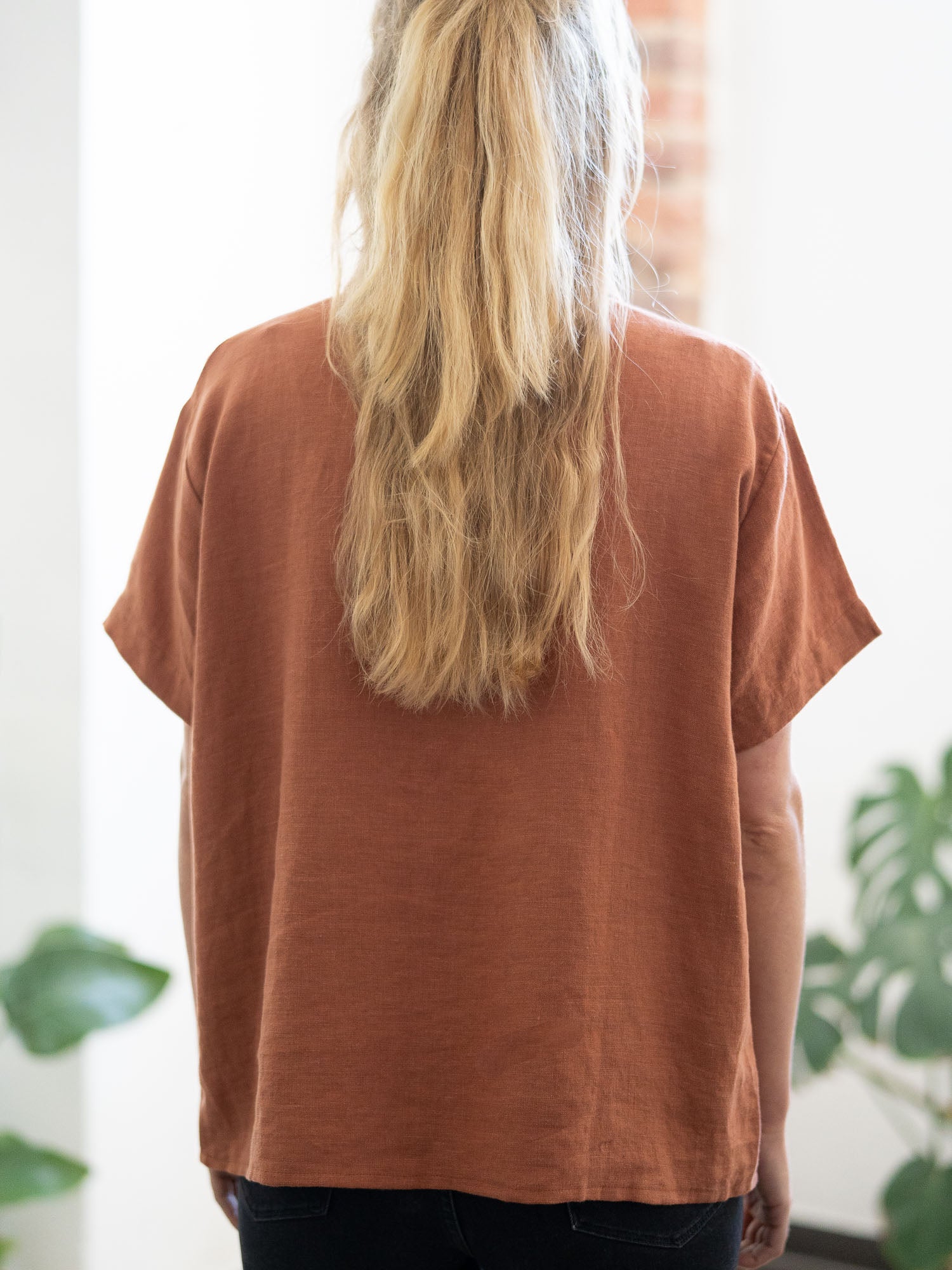 Eine junge, blonde Frau trägt eine nachhaltige Fair Fashion Kurzarm Leinenbluse in rotbraun von FUXBAU.