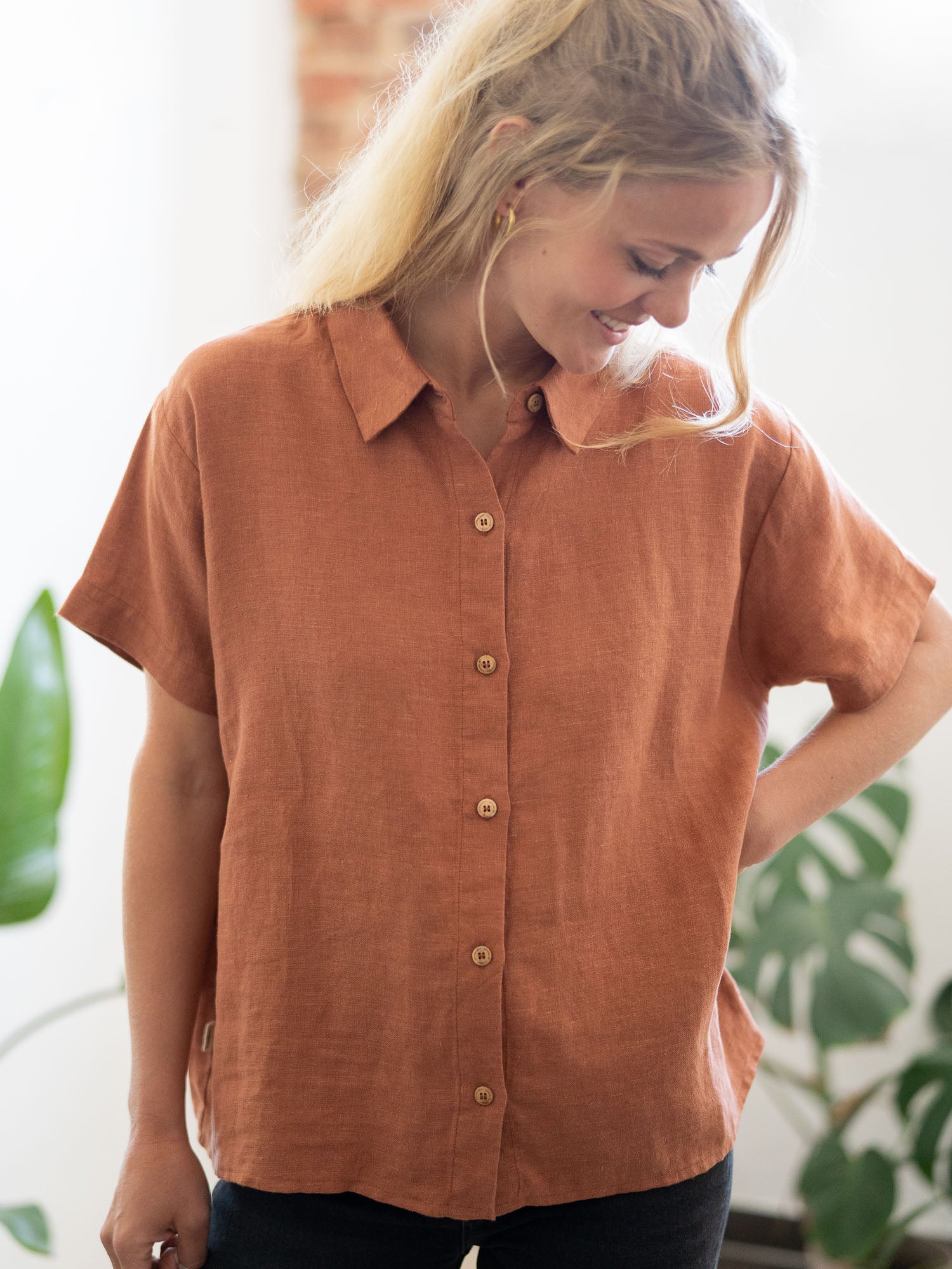 Eine junge, blonde Frau trägt eine nachhaltige Fair Fashion Kurzarm Leinenbluse in rotbraun von FUXBAU.