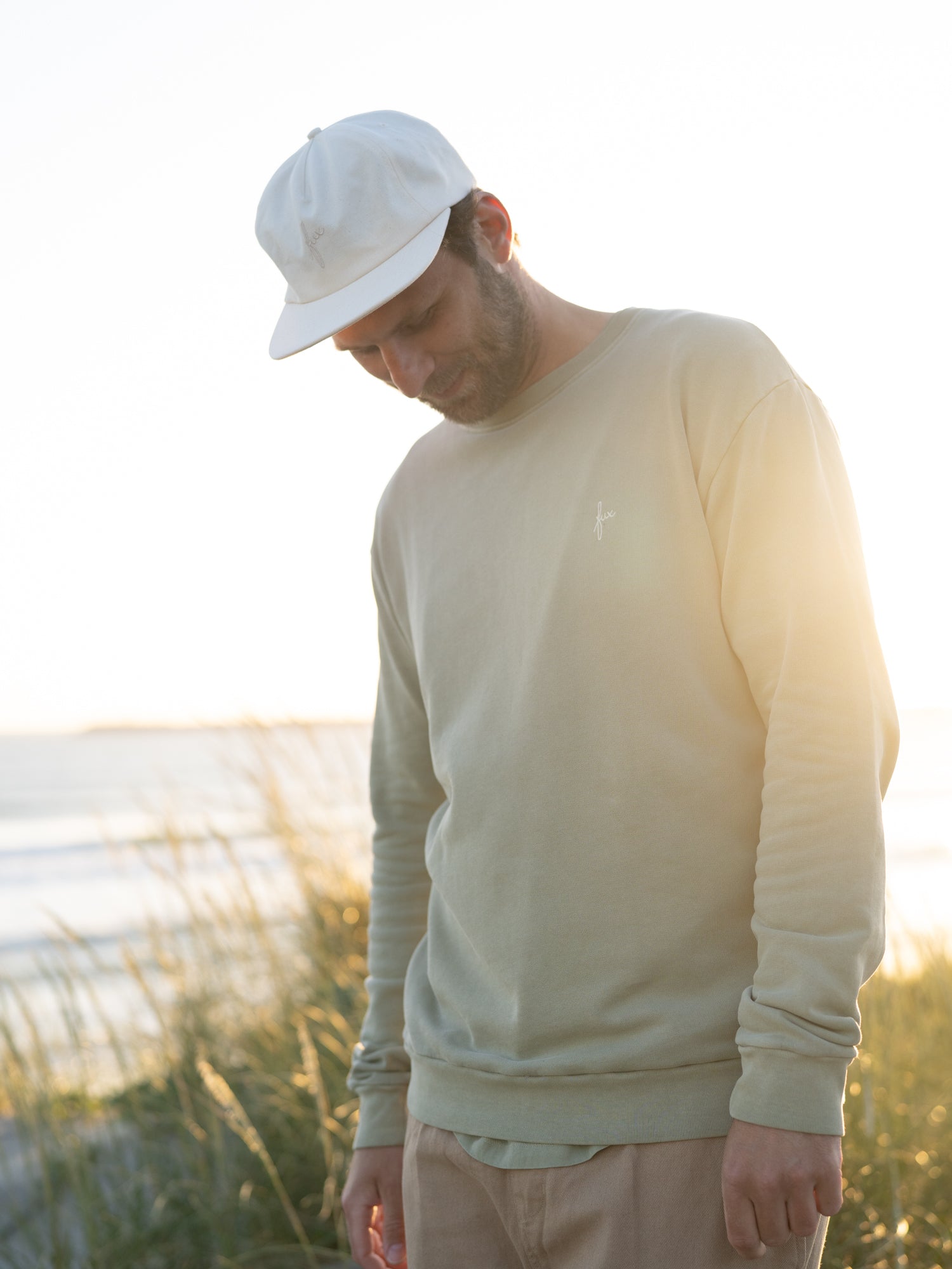 Fair produziertes Männer Sweatshirt seegrün getragen von einem jungen Mann am Meer