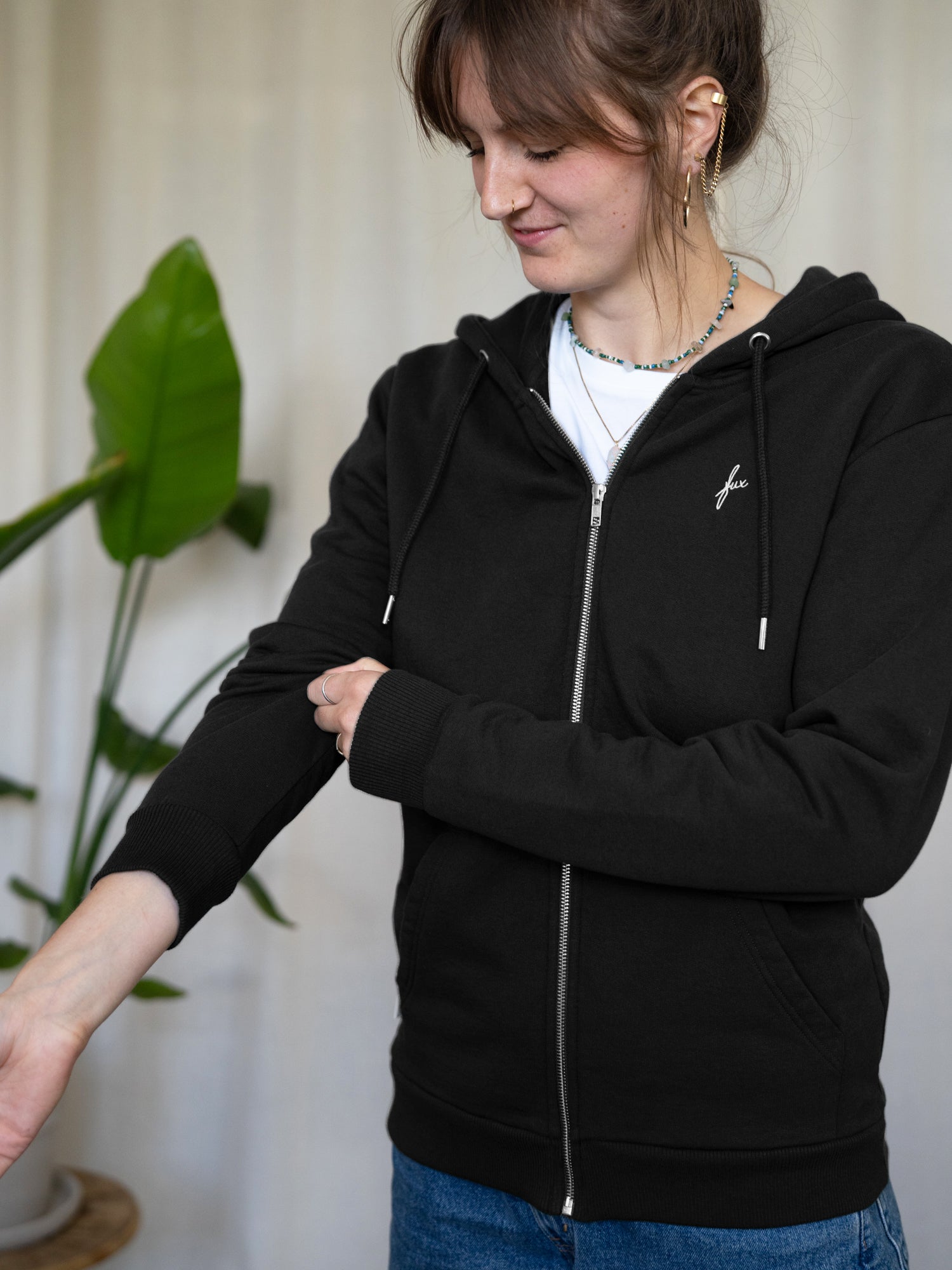 Nachhaltige Unisex Sweatjacke in Schwarz aus Bio-Baumwolle – fair produziert in Portugal - getragen von einem dunkel haarigem weiblichem Modell