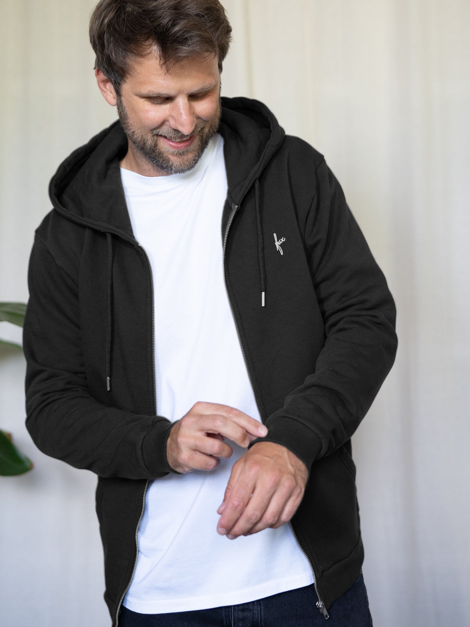 Nachhaltige Unisex Sweatjacke in Schwarz aus Bio-Baumwolle – fair produziert in Portugal - getragen von einem dunkel haarigem männlichem Modell