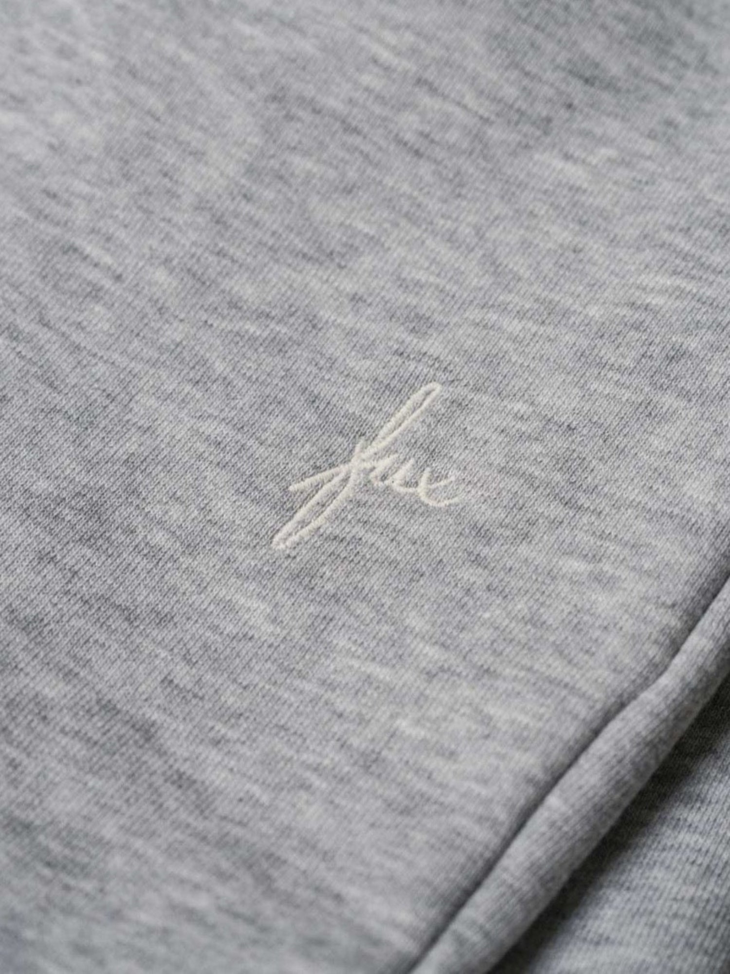 Detailansicht einer nachhaltigen fair fashion Jogginghose von FUXBAU mit weißem fux stick auf grau meliertem Stoff aus Biobaumwolle.