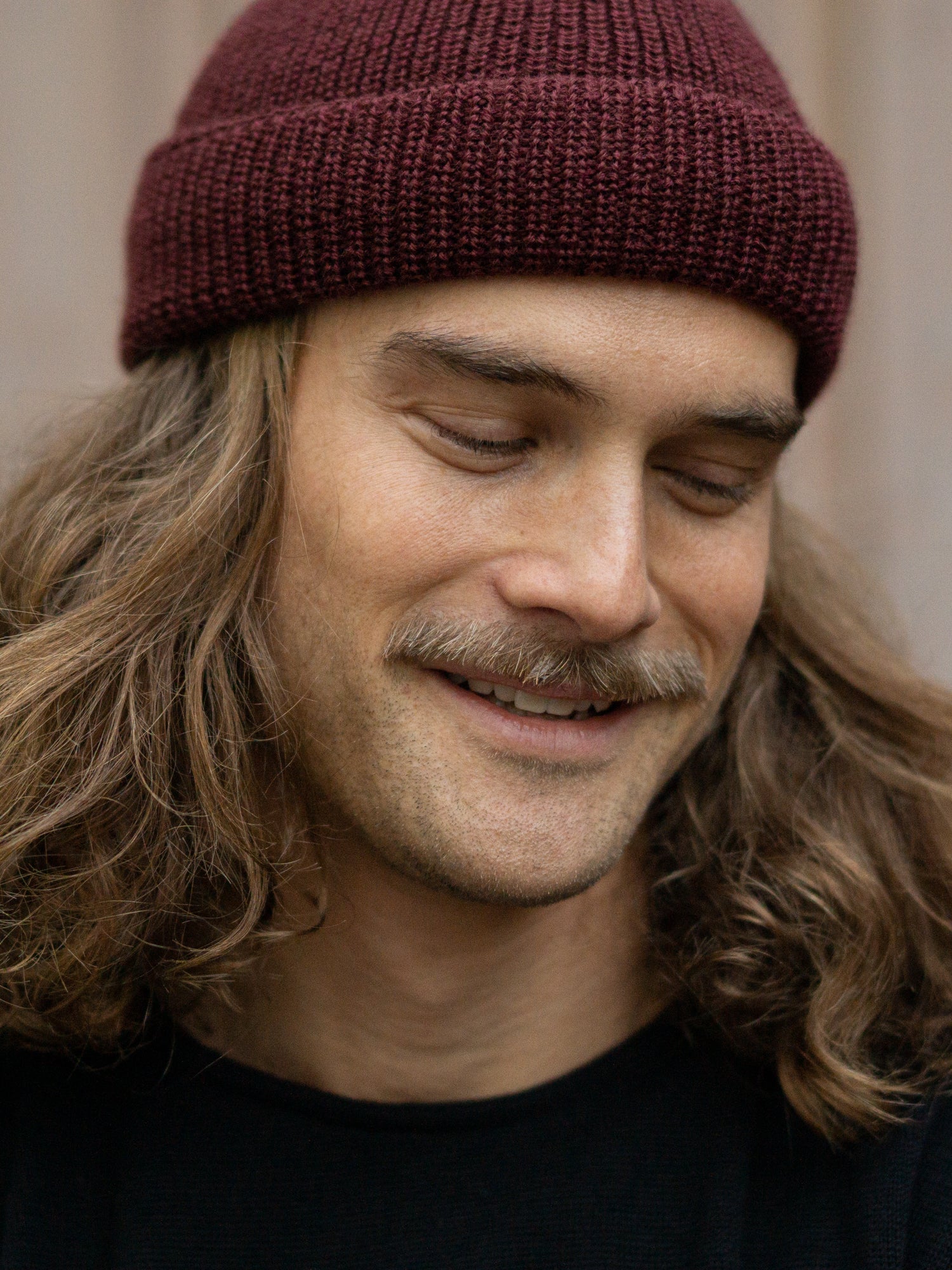Ein junger, braunhaariger Mann trägt eine Merino Fischermütze von FUXBAU aus 100% GOTS zertifizierter Merino Schurwolle in der Farbe Bordeaux. Gestrickt in Deutschland unter fairen und nachhaltigen Bedingungen.