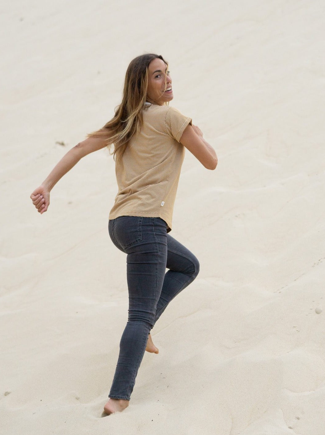 Rachel trägt unser Fair Fashion Streifenshirt in creme senf und rennt am Strand