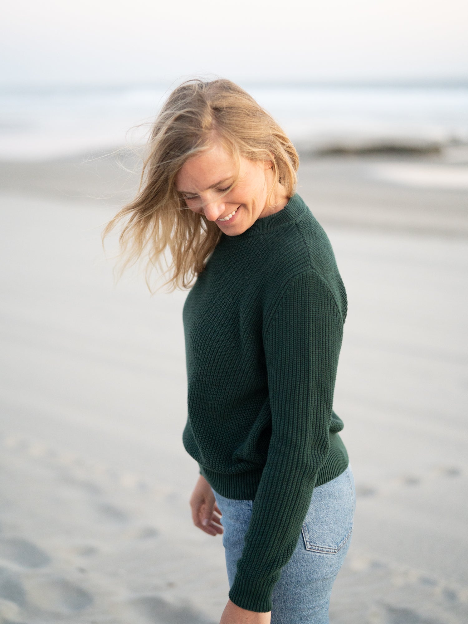 Isi trägt unseren FUXBAU 4Seasons STrickpullover in waldgrün aus 100% GOTS zertifizierter Biobaumwolle am Strand in Portugal.