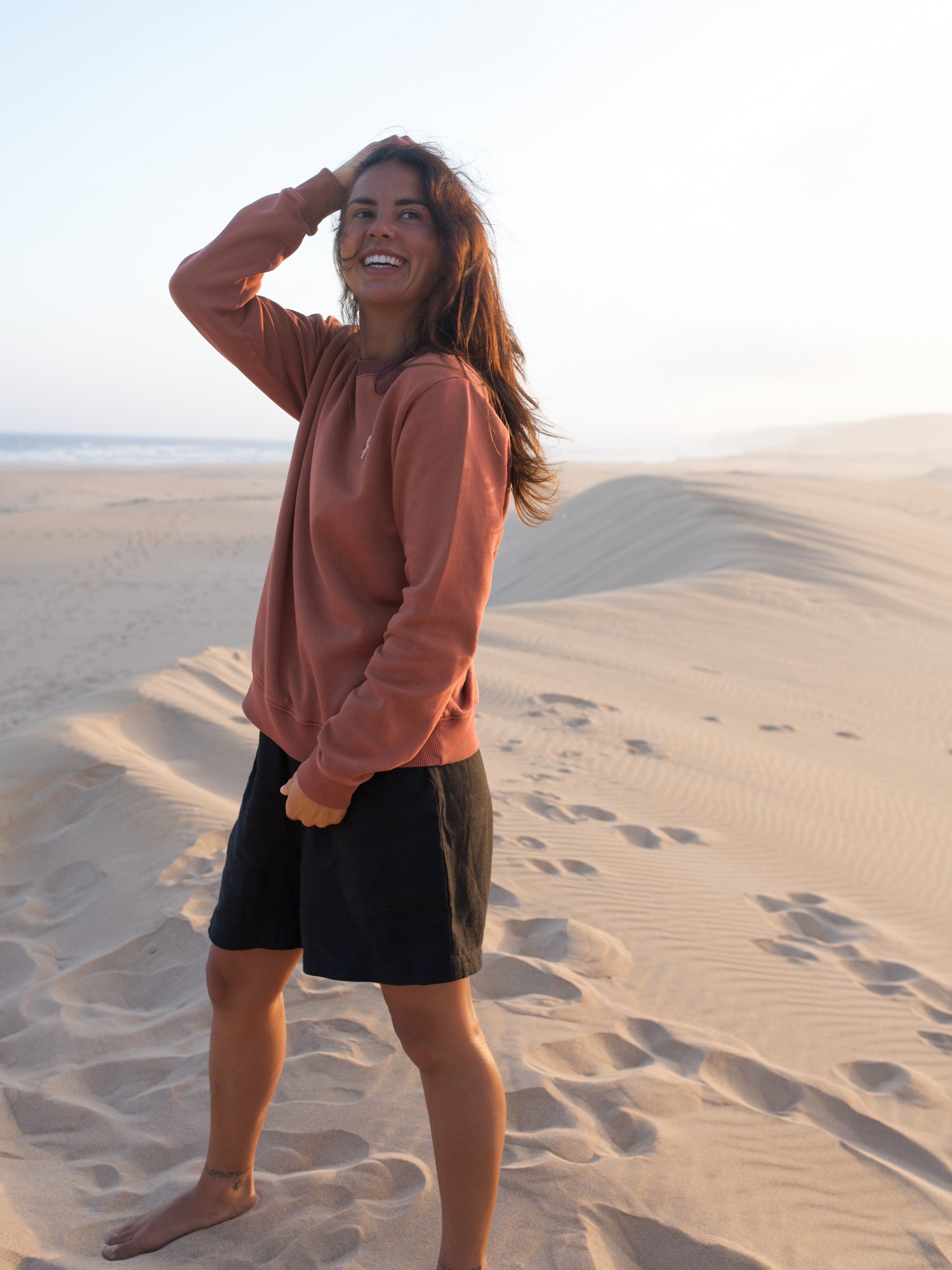 Frau trägt stückgefärbten roten FUXBAU Pullover aus Biobaumwolle am Strand in Portugal