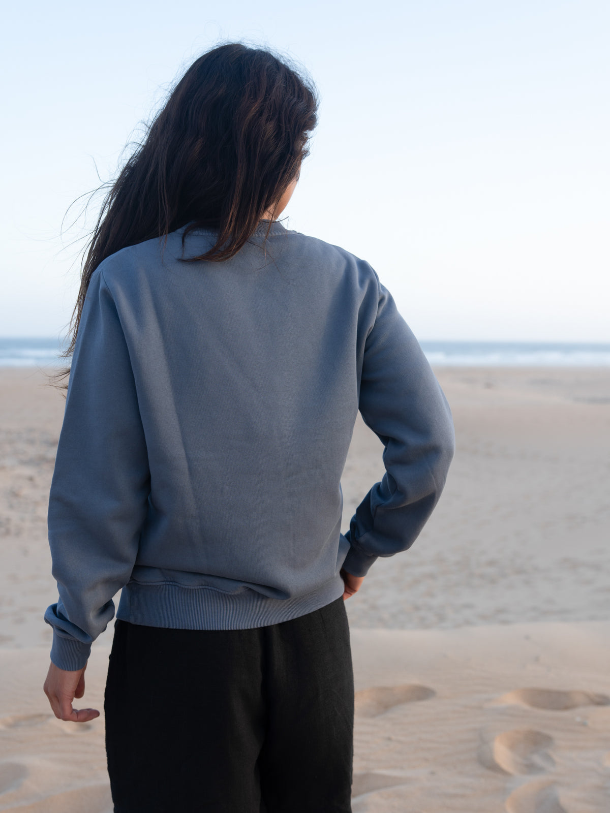 Rückansicht vom seeblauen Frauen Pullover von FUXBAU vor Strand und Meer in Portugal