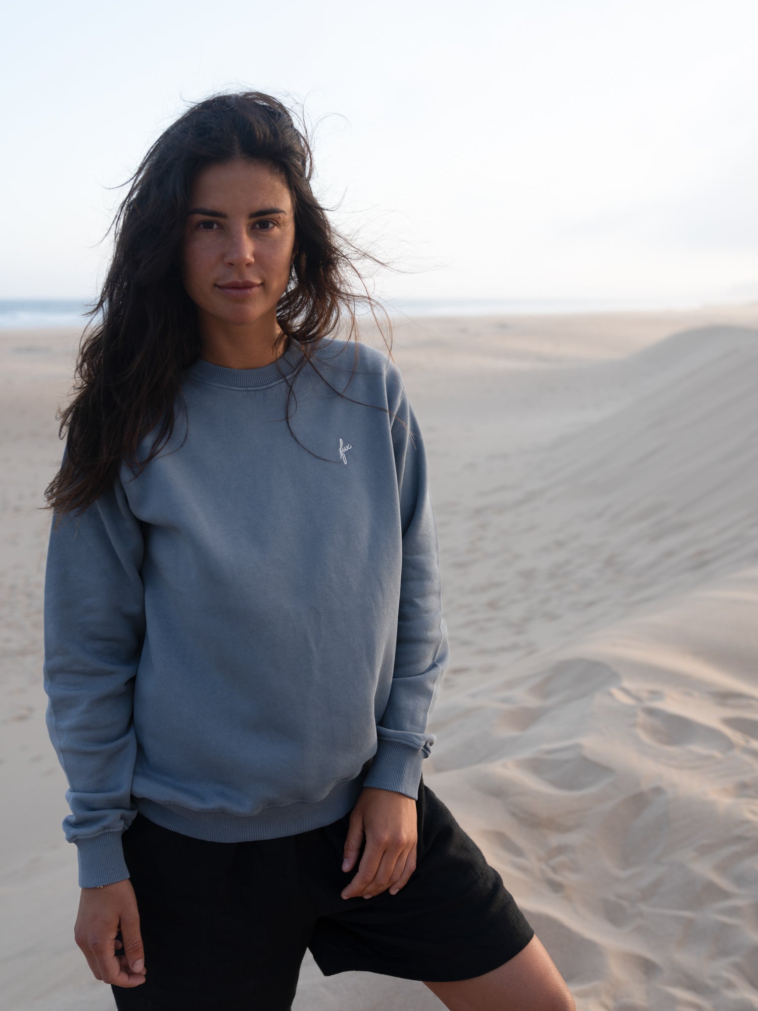 Frau trägt fair gefertigten seeblauen FUXBAU Pullover aus Biobaumwolle in Portugal