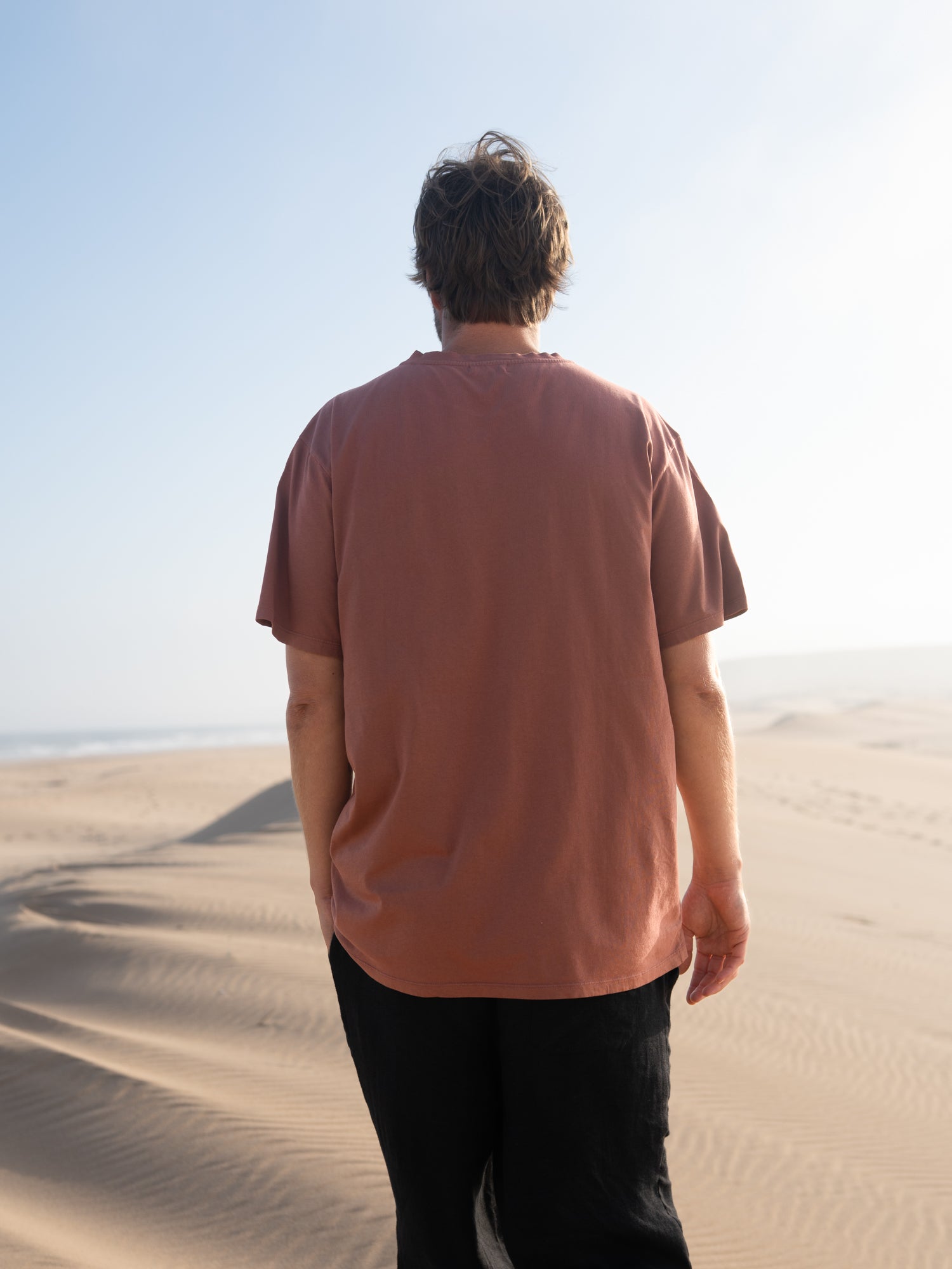 Rückansicht vom roten FUXBAU Männer T-Shirt aus Biobaumwolle in den Dünen