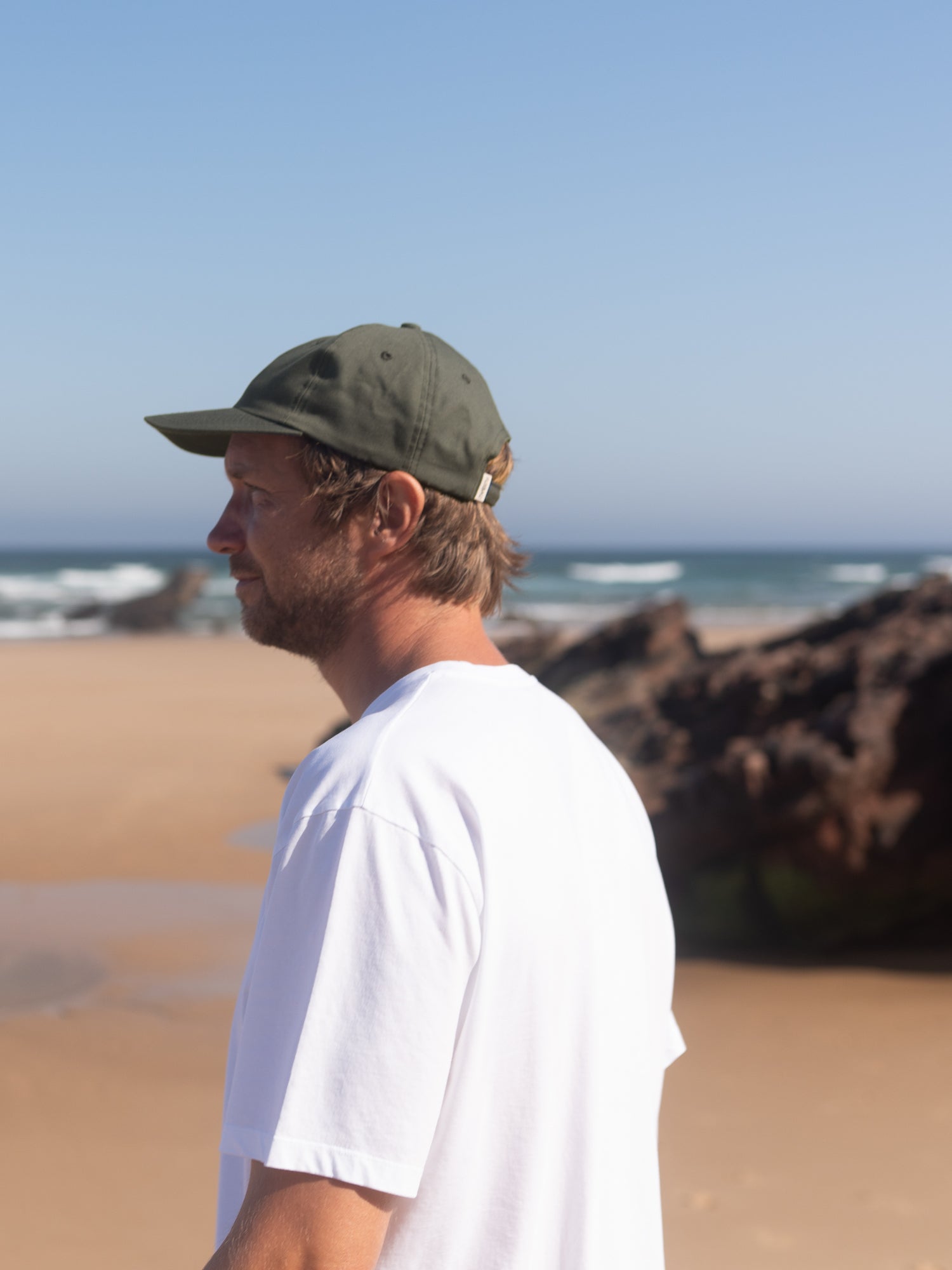 Mann trägt nachhaltige olivgrüne Dad Cap aus Biobaumwolle am Strand