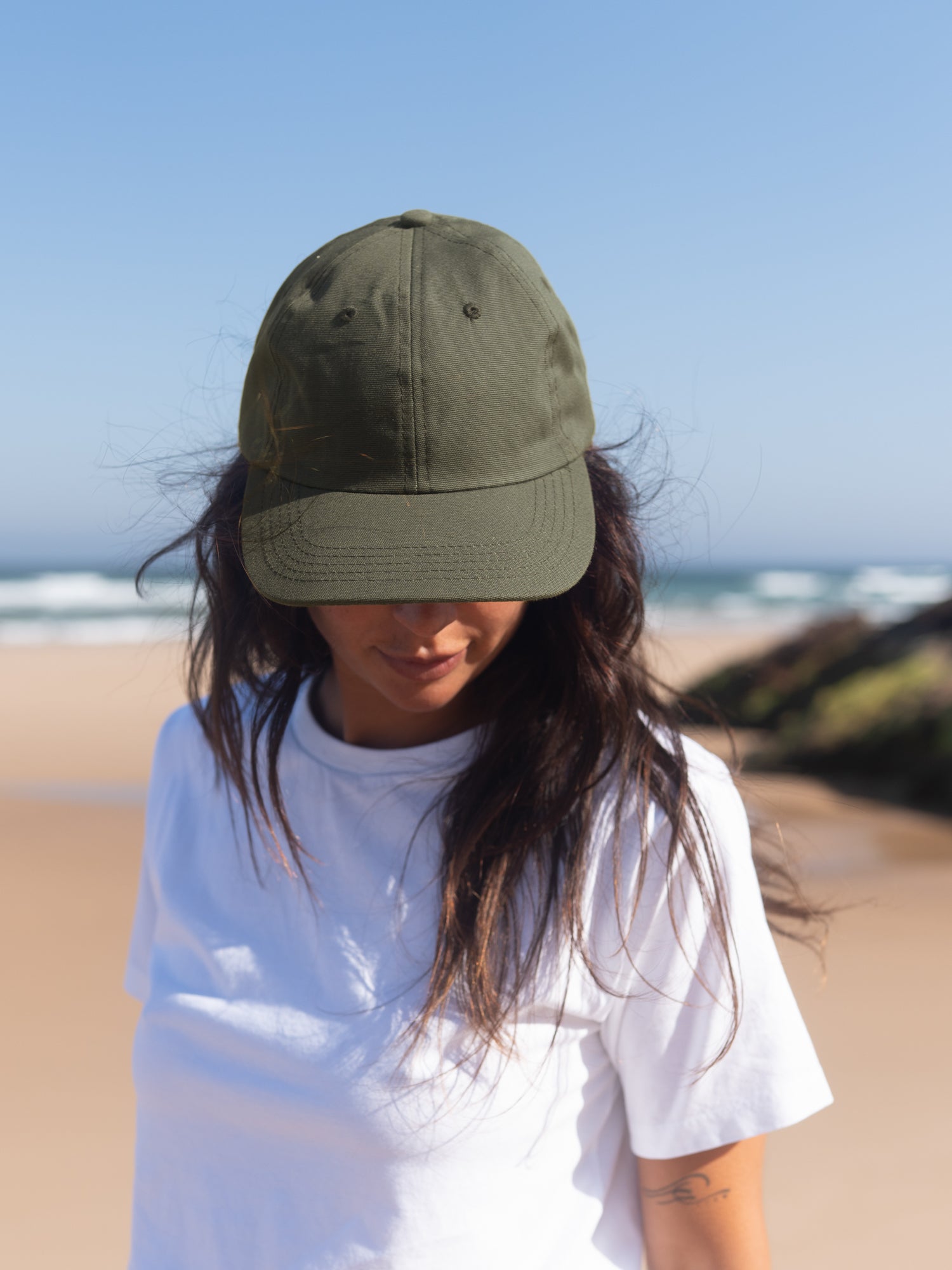 Frau trägt olivgrüne Dad Cap aus Biobaumwolle am Strand mit Blick nach unten