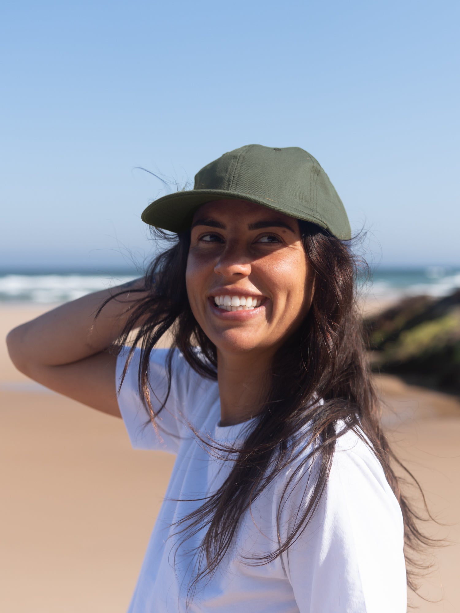 Frau trägt nachhaltige olivgrüne Dad Cap aus Biobaumwolle am Strand