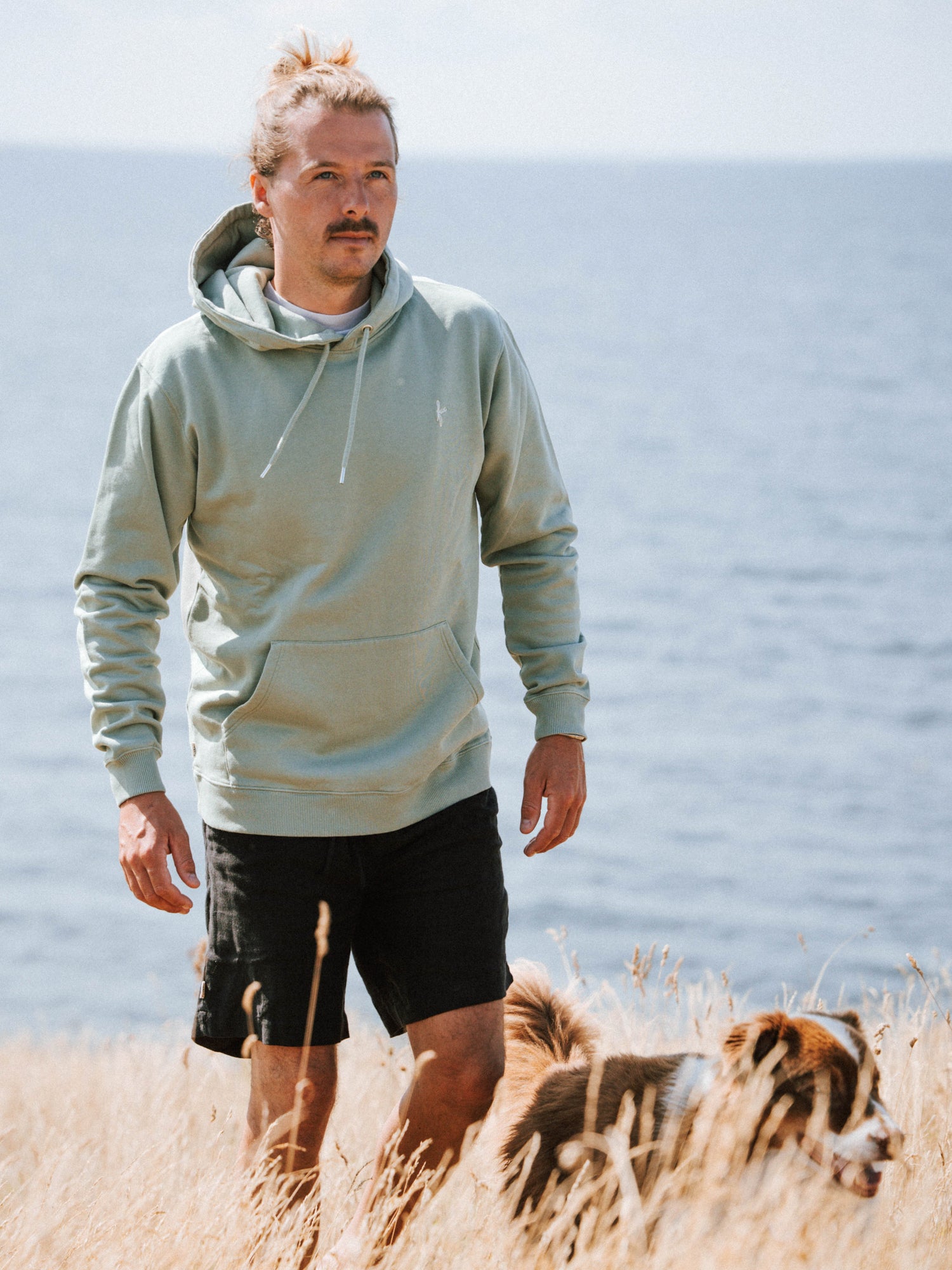 Unisex Hoodie in Seegras aus Biobaumwolle getragen von einem Mann am Meer