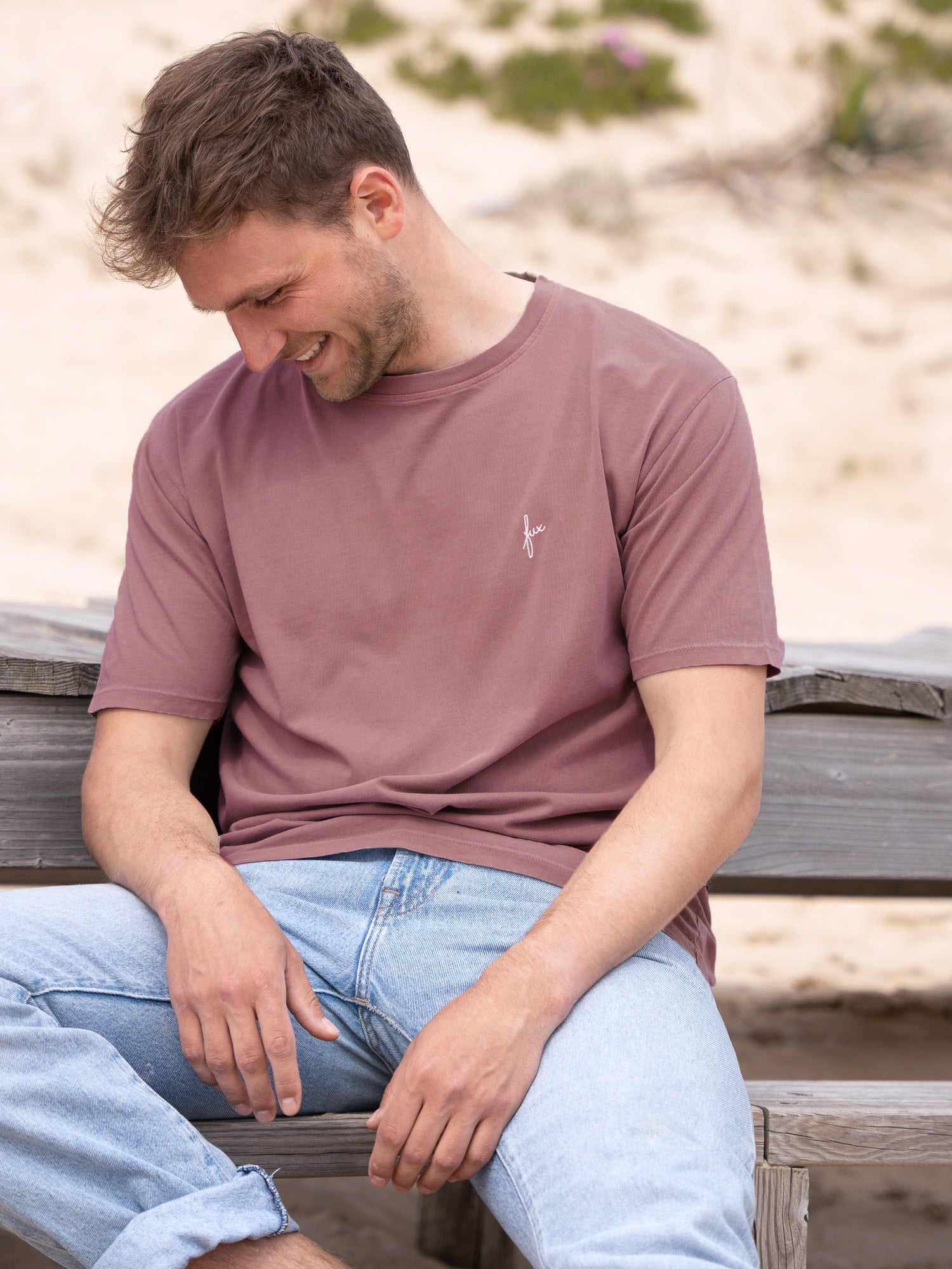 Fuxbau Fair Fashion Männer Natural Dye T-Shirt rot aus 100% Biobaumwolle. Gefertigt unter fairen und nachhaltigen Bedingungen in Portugal und gefärbt mit natürlichen Farbigmenten. Getragen von einem jungen, bloden Mann am Strand in Frankreich.