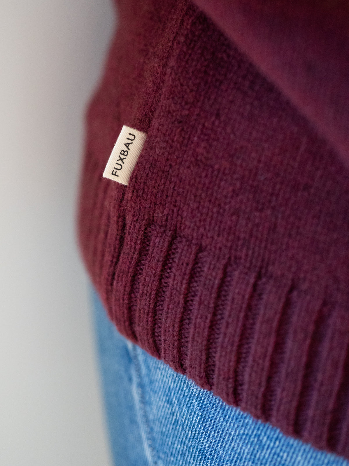 Frauen Strickpullover bordeaux aus 100% Merinowolle, gestrickt in Deutschland – Detailansicht von geripptem Saumbund und seitlichem FUXBAU Label