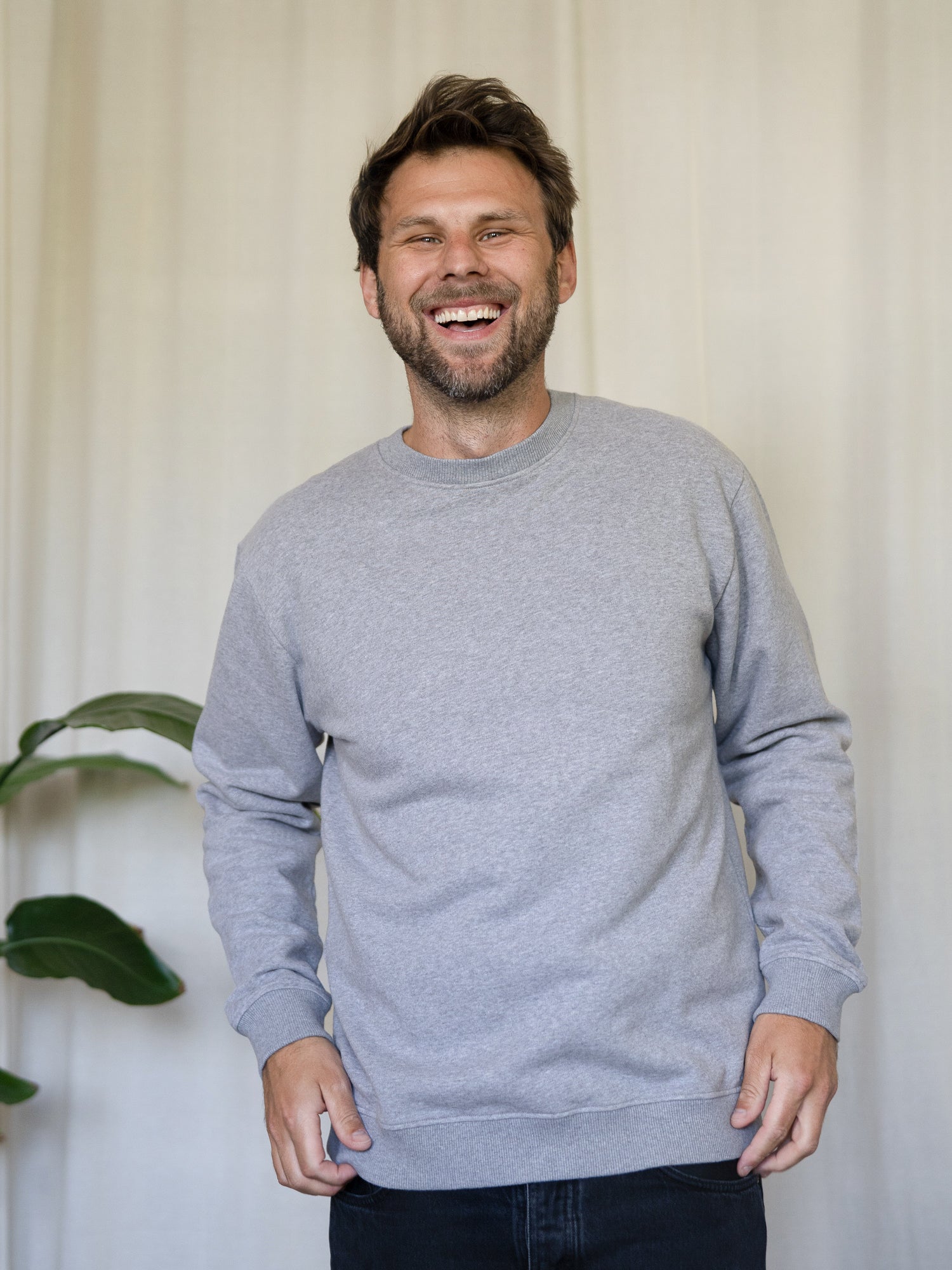 Männer Basic Sweater graumeliert – Modell lacht und trägt den zeitlosen Pullover aus 100% GOTS-zertifizierter Biobaumwolle, fair in Portugal hergestellt