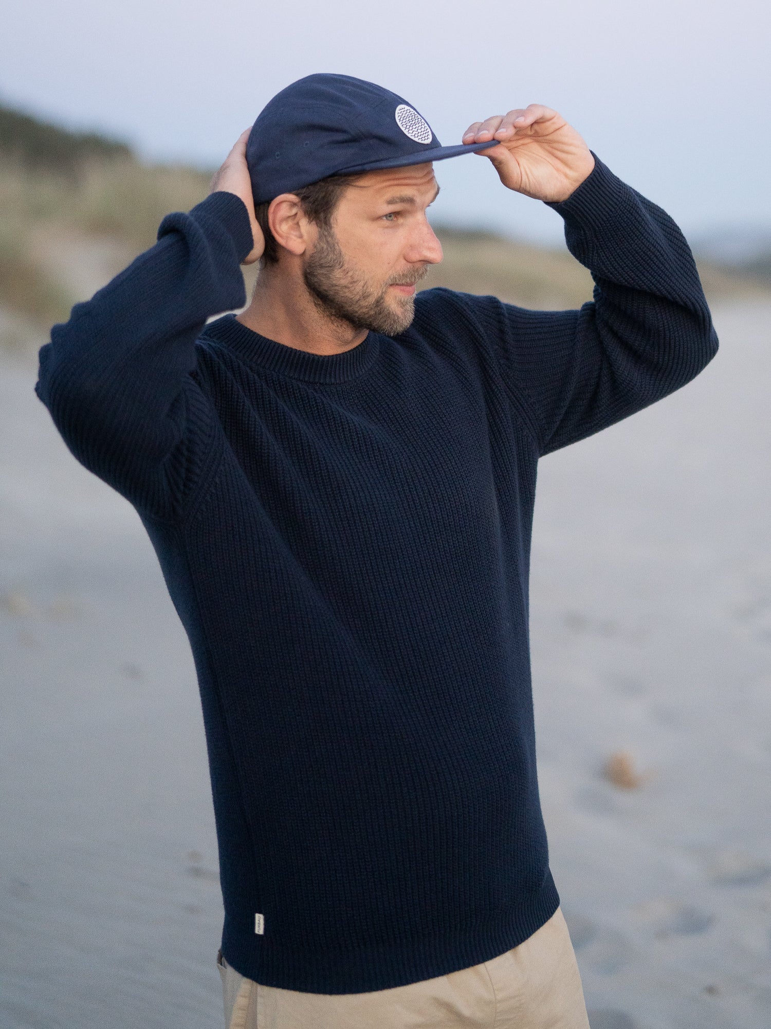 FUXBAU 4Seasons Männer Strickpullover in navy aus 100% GOTS zertifizierter Biobaumwolle, getragen am Strand in Nordportugal vor Sonnenuntergang.