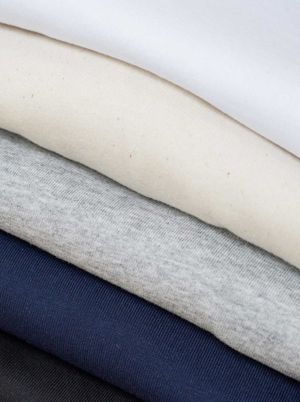 Stapel verschieden farbiger Basic T-Shirts von FUXBAU aus 100% nachhaltiger Biobaumwolle in weiß, natur, grau, navy und schwarz