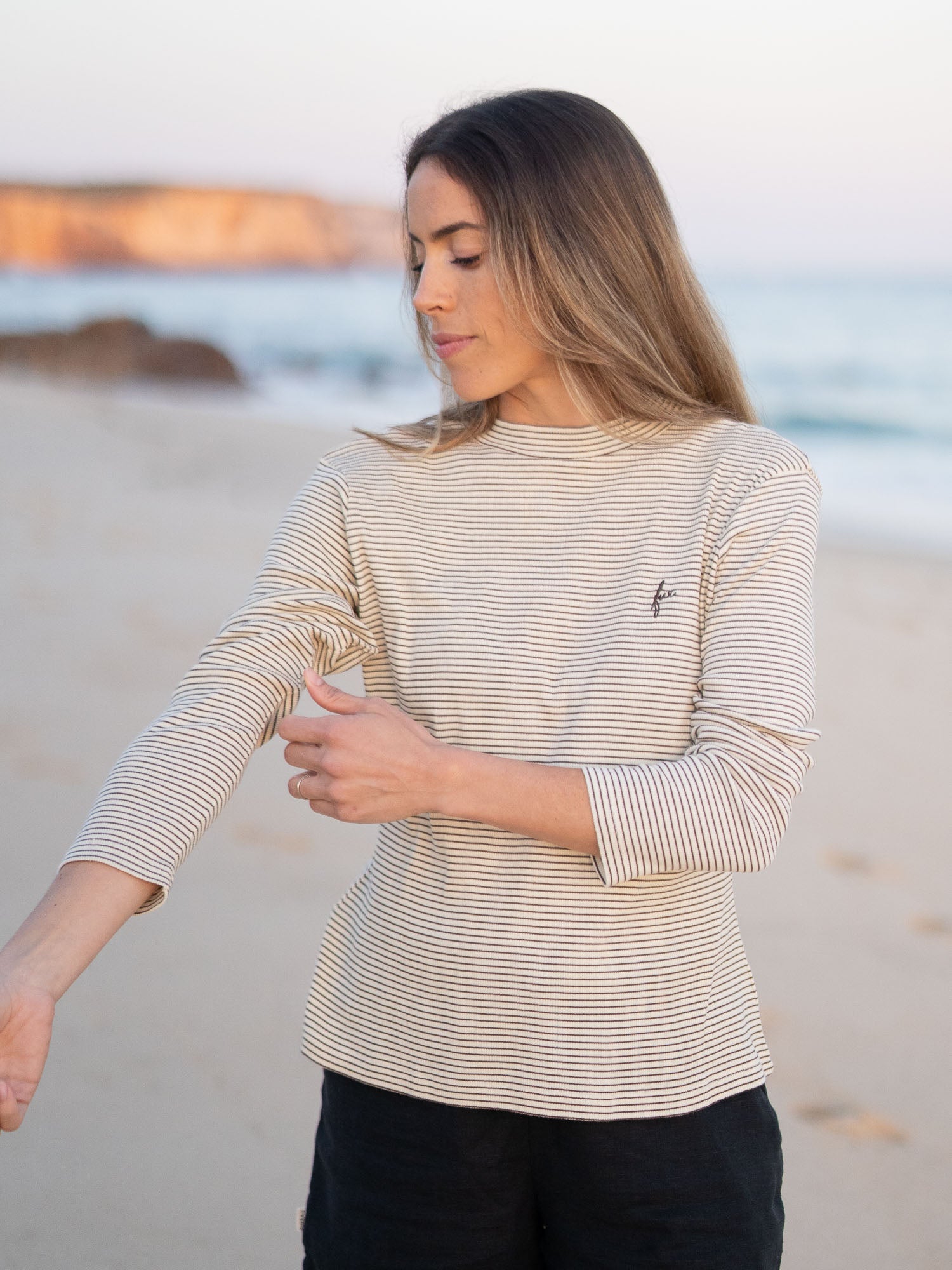 Nachhaltiges FUXBAU Fair Fashion fitted Stehkragen longsleeve creme braun gestreift aus GOTS zertifzierter Biobaumwolle Made in Portugal getragen am Strand in Portugal.