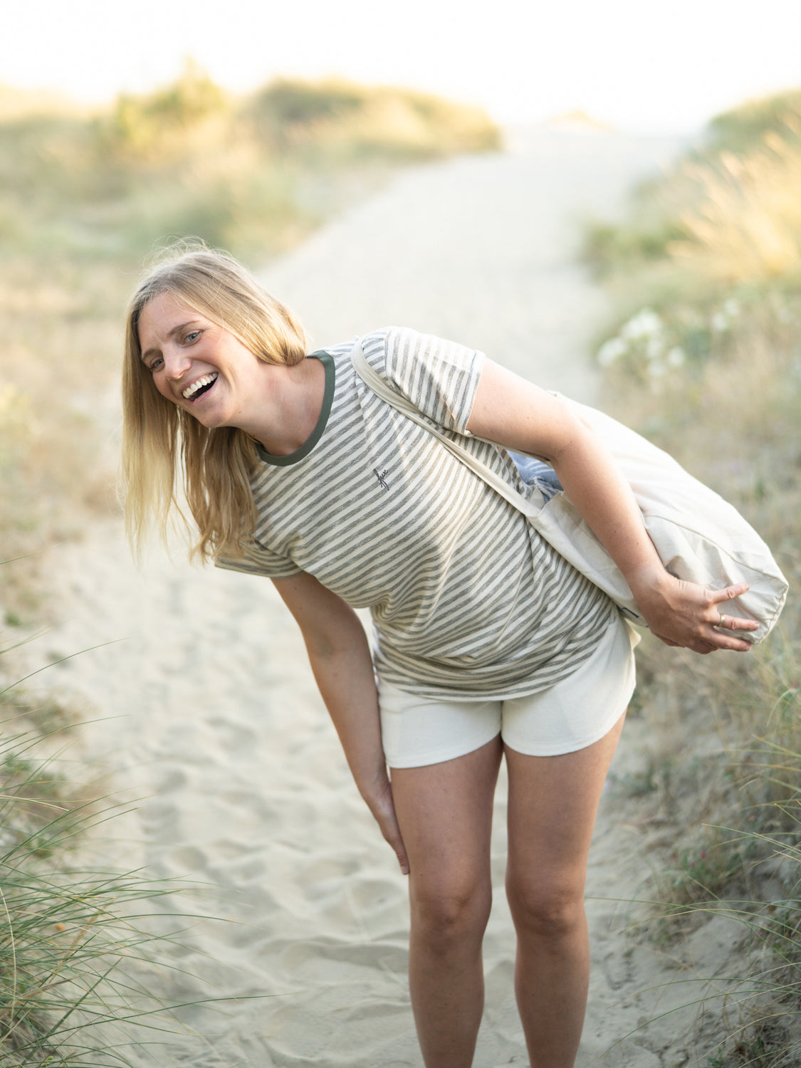 Junge, blonde Frau trägt ein FUXBAU Frauen Merida fux T-Shirt in beige grünmeliert am Strand in Portugal und lacht herzlich.