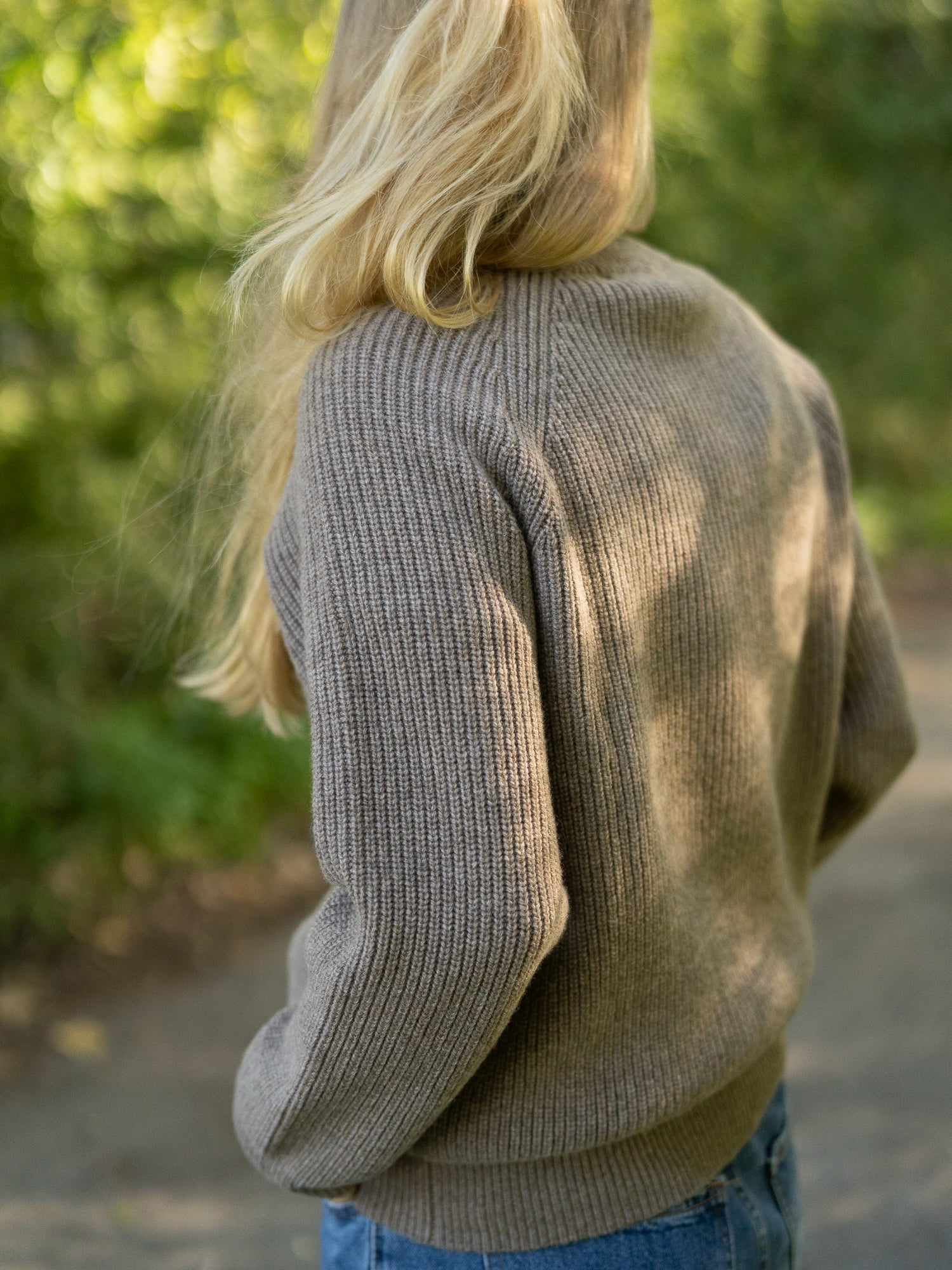 Nachhaltiger Fair Fashion Frauen Merino Troyer in braun meliert aus 100% Merino Schurwolle Made in Italy, getragen von einer jungen Frau mit einer Rückansicht.