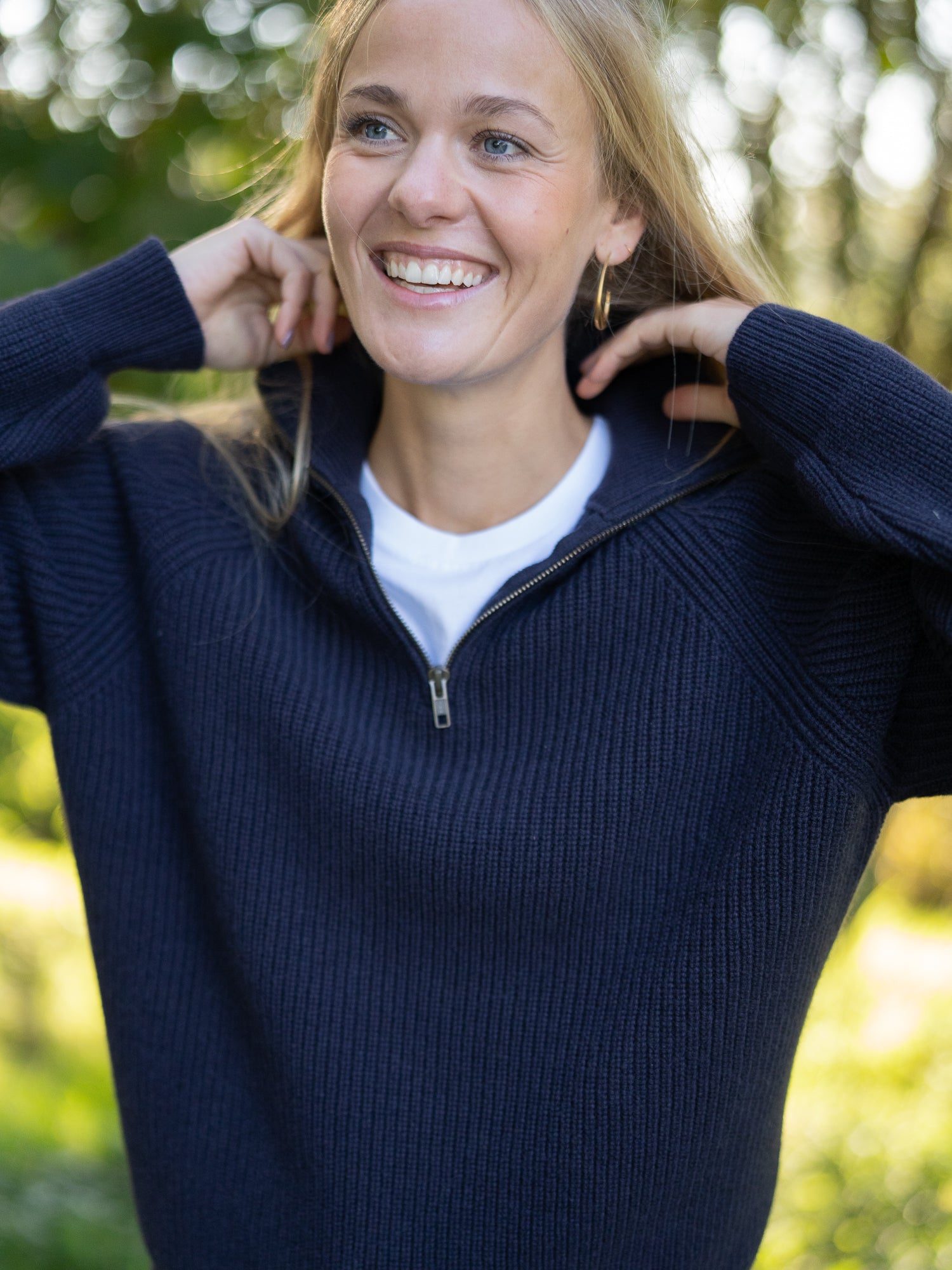 Nachhaltiger Fair Fashion Frauen Merino Troyer in navy aus 100% Merino Schurwolle in navy Made in Italy, getragen von einer jungen Frau die die Hand am kragen hat.