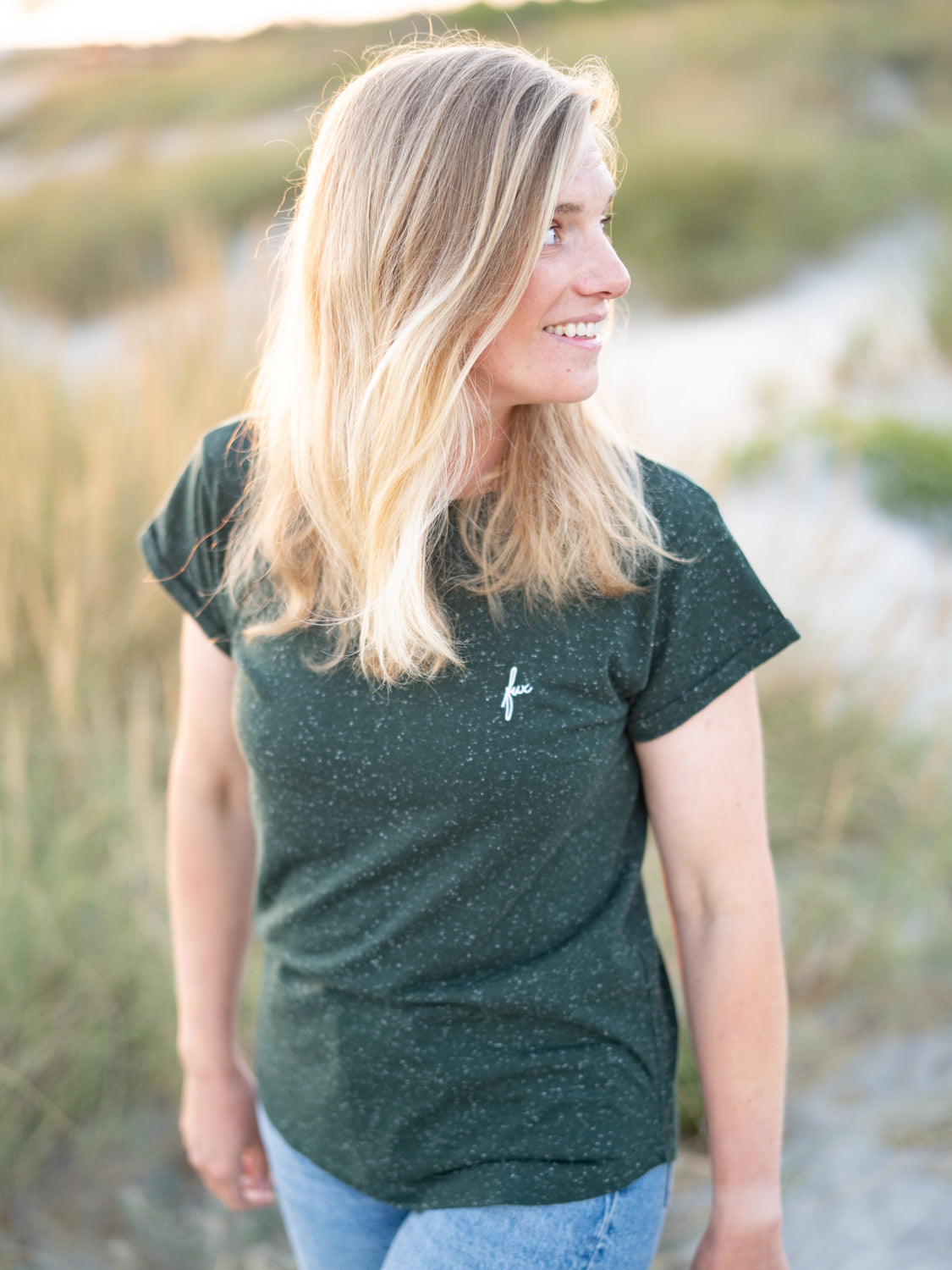 FUXBAU Fair Fashion Frauen T-Shirt in grün aus Biobaumwollen mit weißen Punkten getragen von einer jungen blonden Frau am Strand.