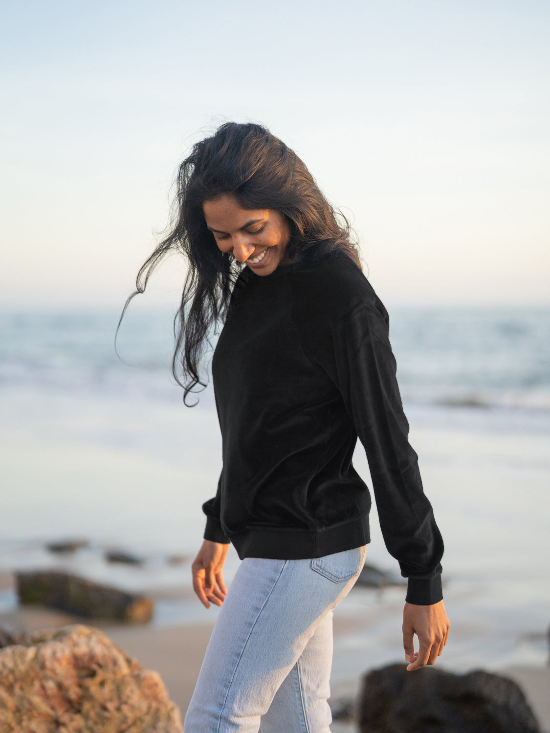 Neelia trägt den FUXBAU Fair Fashion Frauen Samt Sweater in schwarz am Strand aus 100% Biobaumwolle, GOTS und made in Portugal