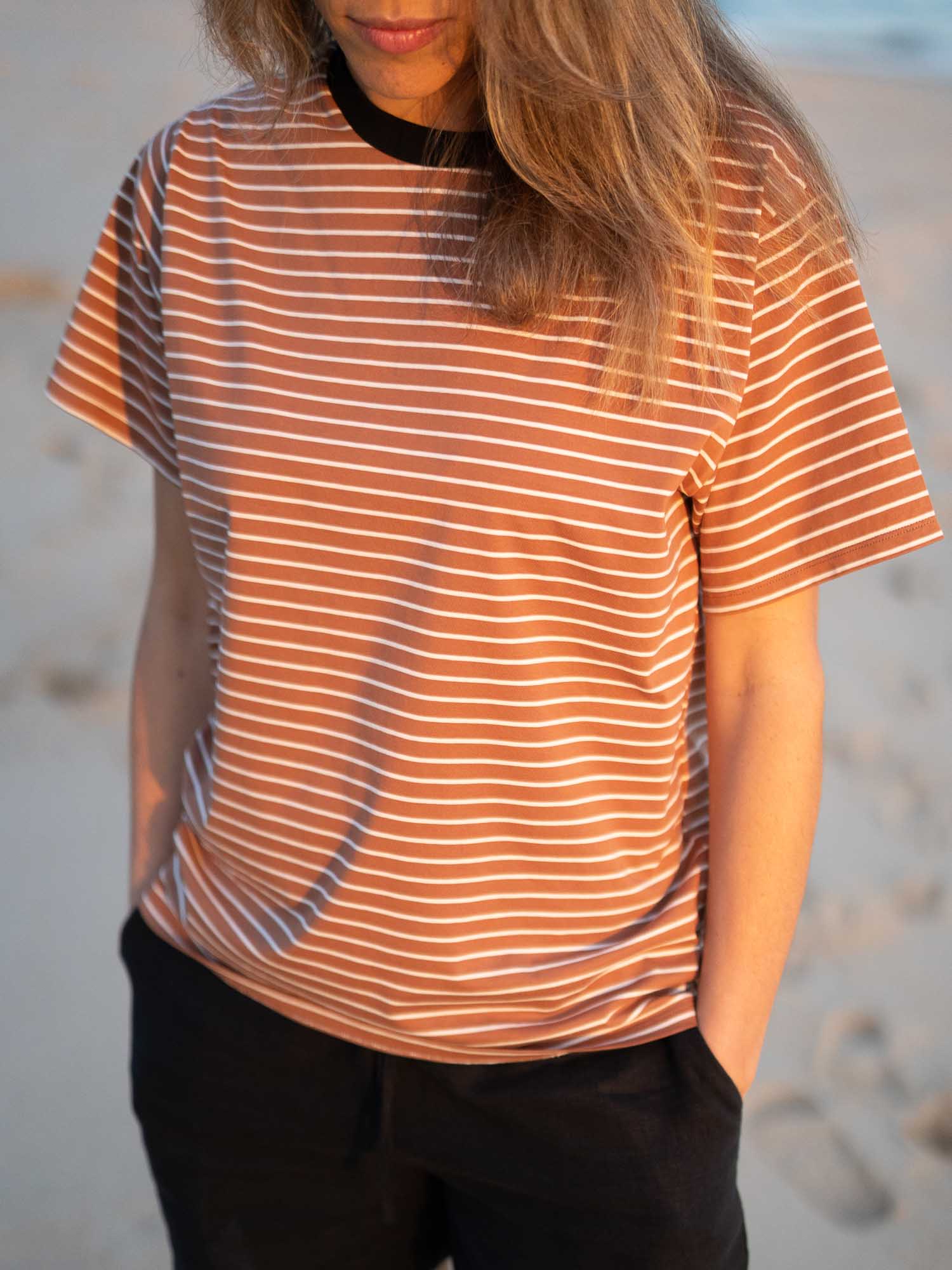 Detailansicht eines Fair Fashion Frauen T-Shirt in karamell, schwarz und weiss von FUXBAU aus Biobaumwolle. Gefertigt unter nachhaltigen GOTS Bedingungen in Portugal und getragen am Strand in Portugal. Getragen von einer jungen Frau am Strand in Südportuga an der Algarve.