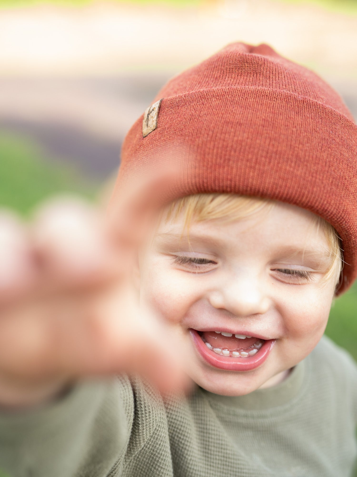 Frontalaufnahme eines lachenden Kindes mit herbstorangener FUXBAU Kinder Merino Kork Beanie – nachhaltige Mütze aus 100% Merinowolle, fair produziert in Deutschland.