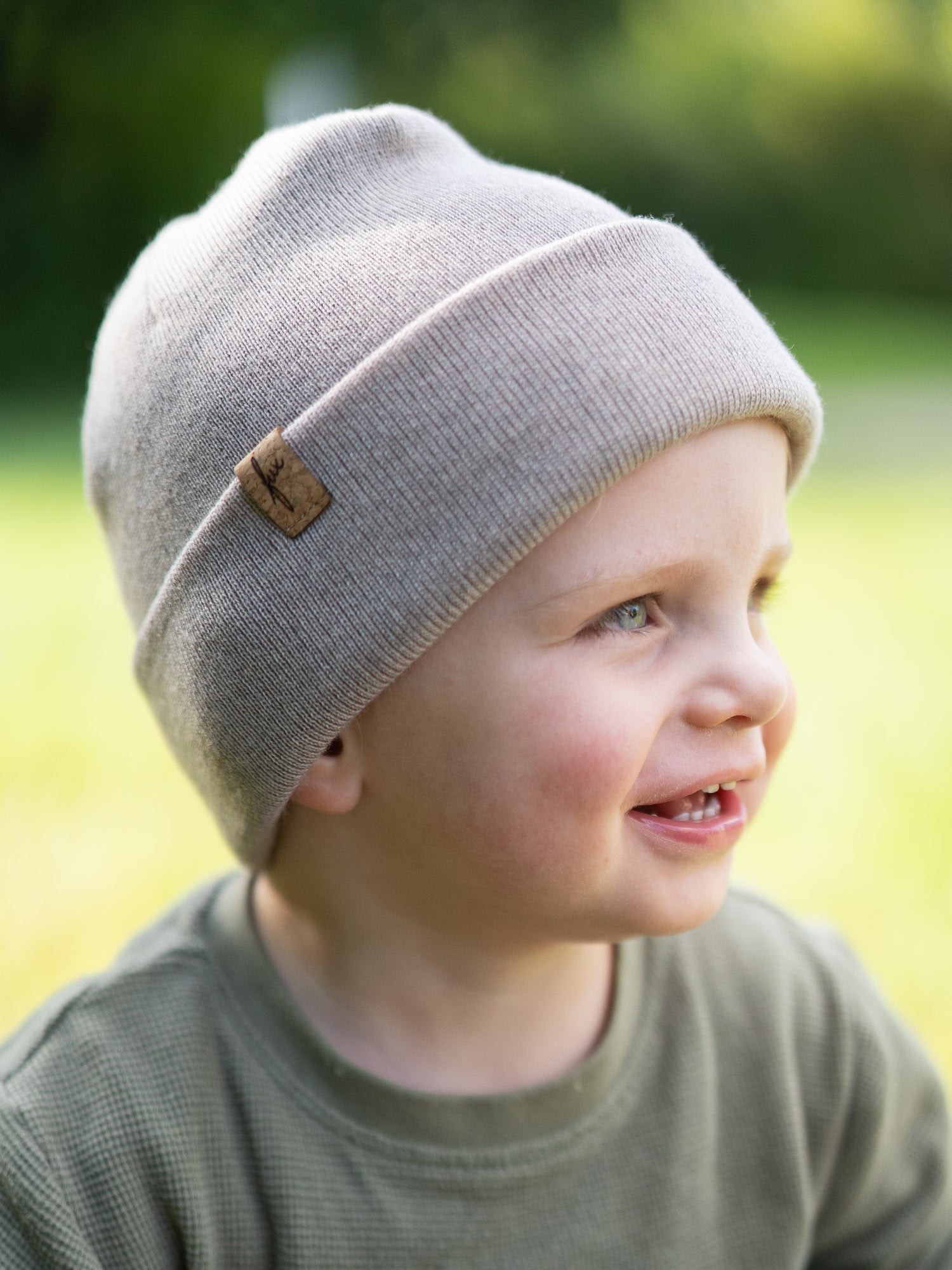 Kind trägt die sandfarbene Kinder Merino Kork Beanie von FUXBAU – fair hergestellt in Deutschland aus weicher Merinowolle, seitliche Ansicht im Freien.