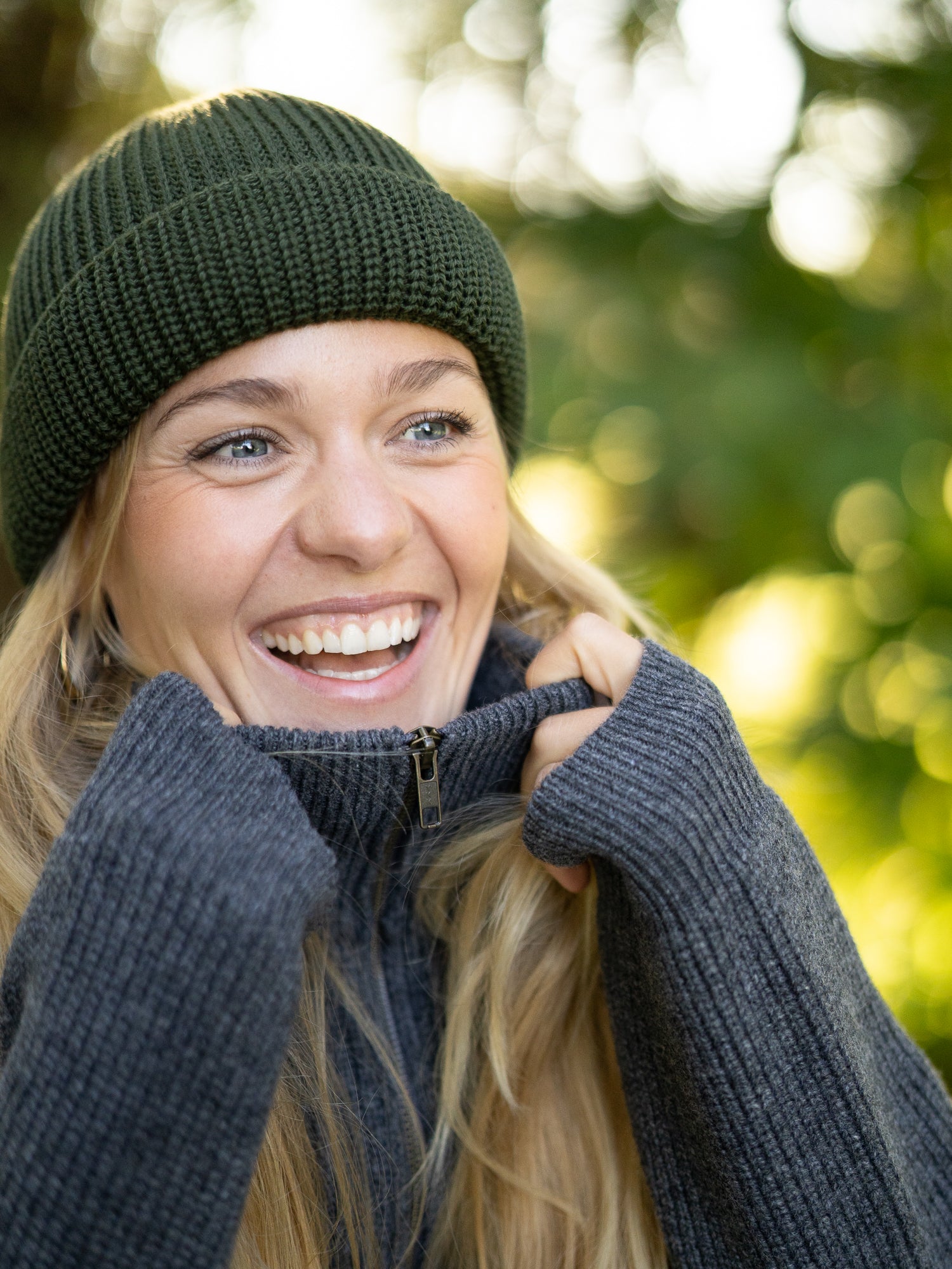 Frau trägt waldgrüne FUXBAU Merino Fischermütze und grauen Strickpullover – nachhaltige, fair gefertigte Mütze aus 100 % Wolle