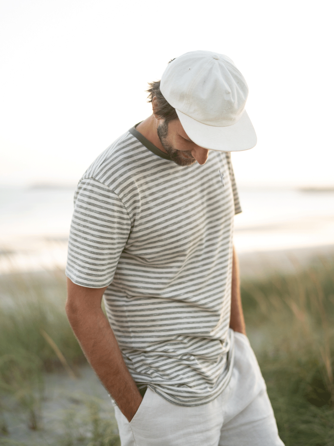Junger Mann trägt ein nachhaltiges FUXBAU Männer Merida T-Shirt in beige grünmeliert gestreift am Strand in Portugal.
