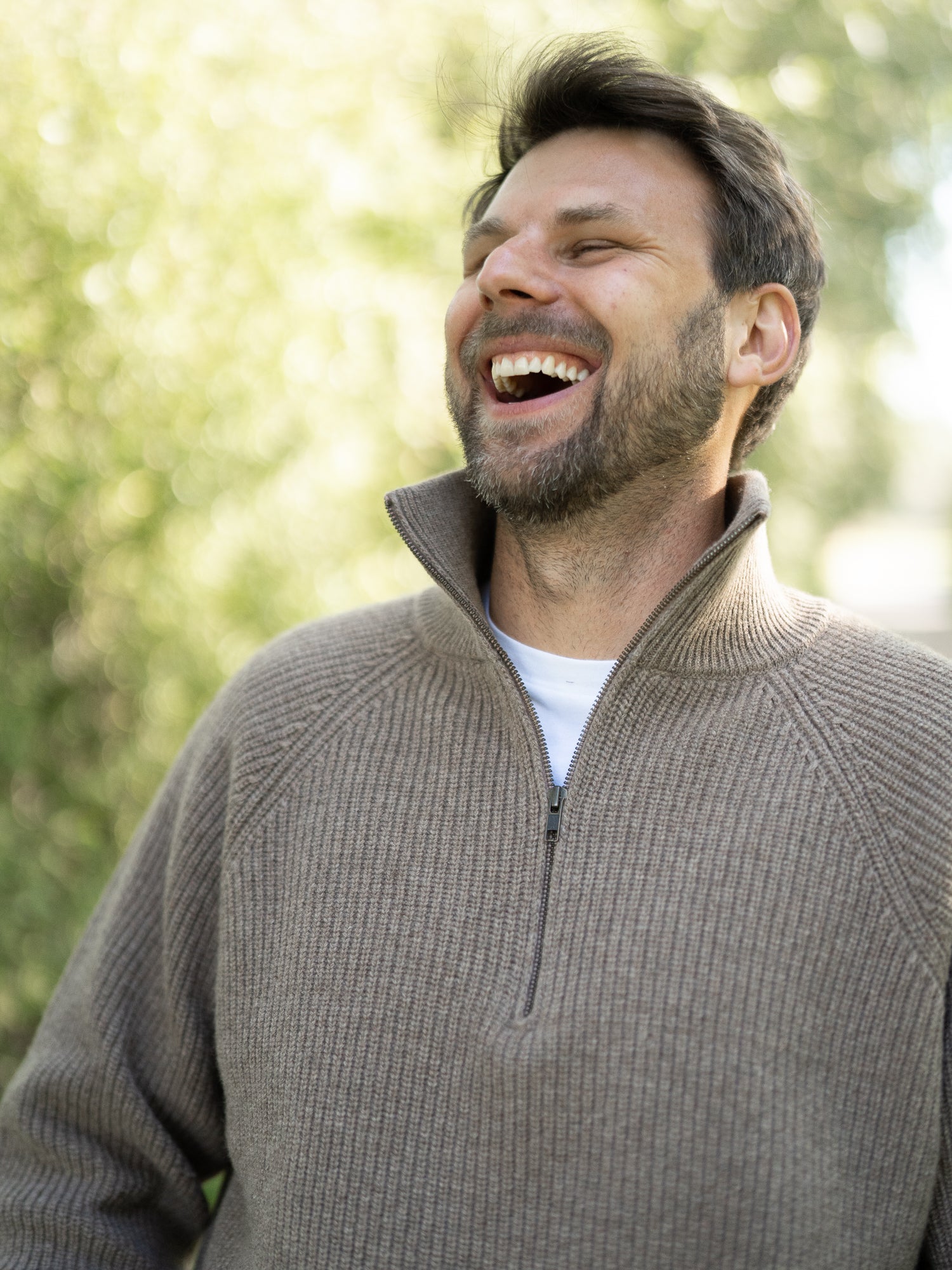 Nachhaltiger Fair Fashion Männer Merino Troyer in braun meliert aus 100% Merino Schurwolle Made in Italy, getragen von einem jungen Mann der in die Kamera seitlich lacht.