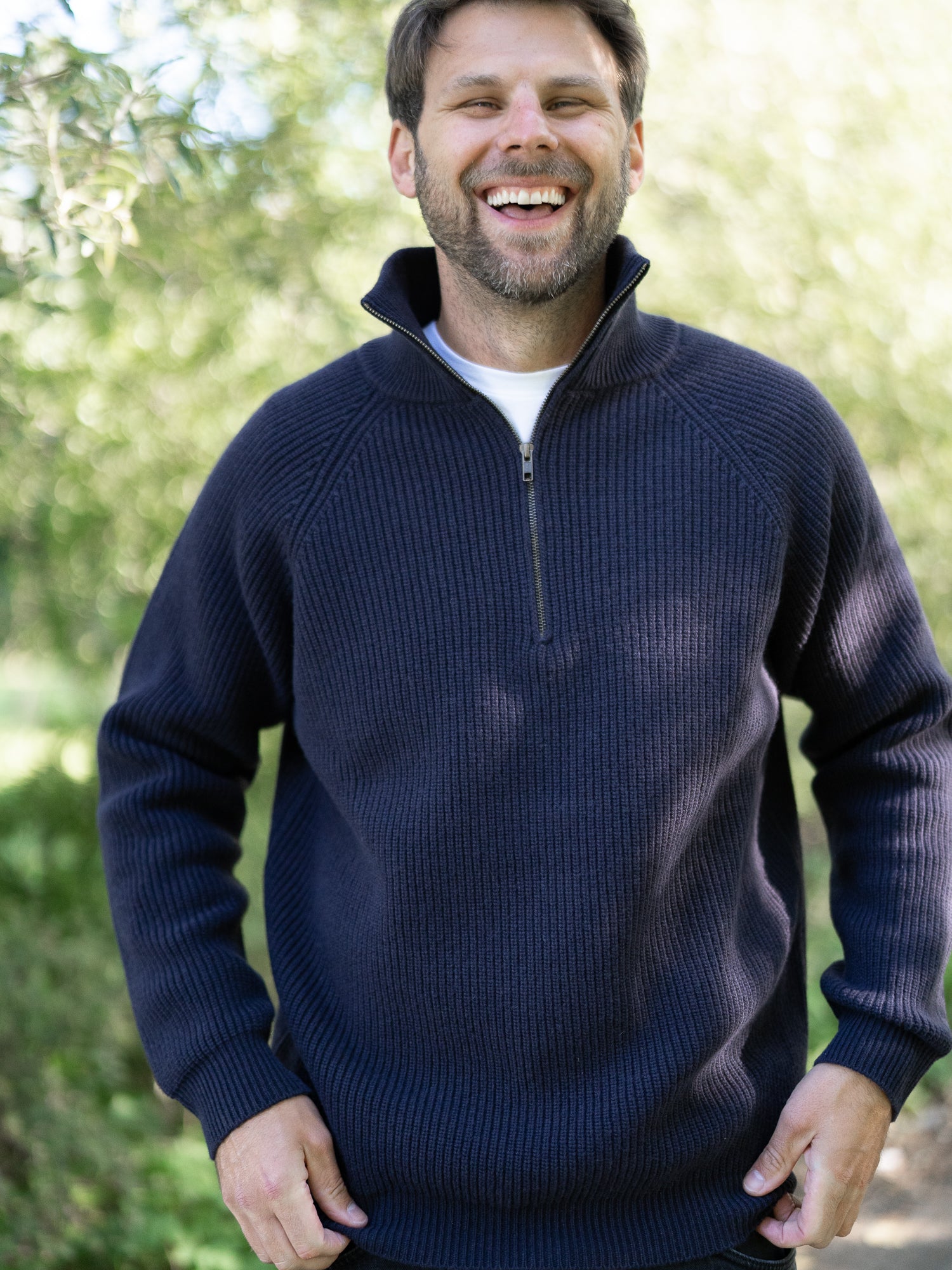 Nachhaltiger Fair Fashion Männer Merino Troyer in navy aus 100% Merino Schurwolle in navy Made in Italy, getragen von einem jungen Mann der frontal in die Kamera lacht. 