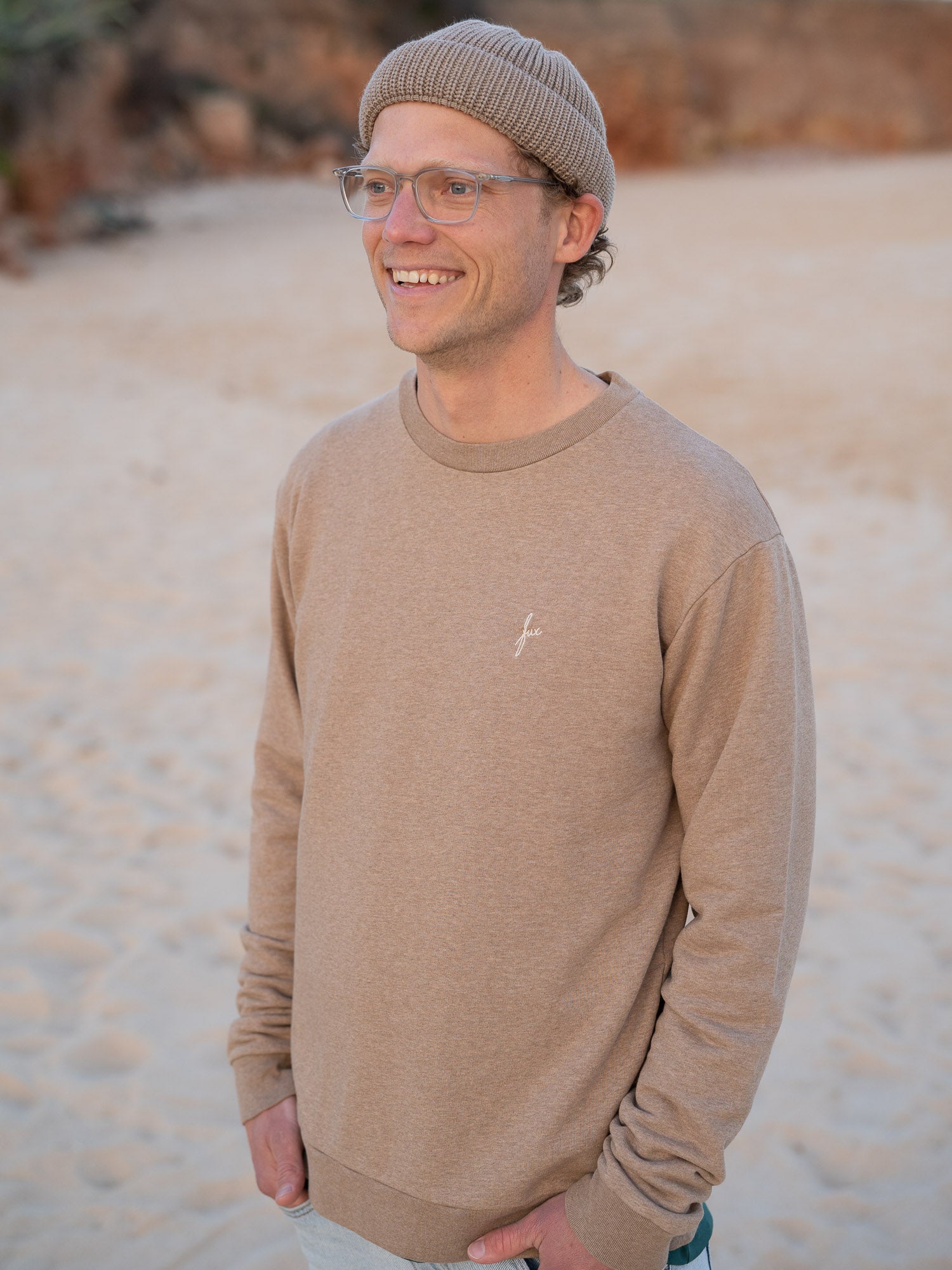 Nachhaltiger Fair Fashion Männer fux Sweater in beige meliert von FUXBAU aus 100% Biobaumwolle getragen am Strand in Portugal. 