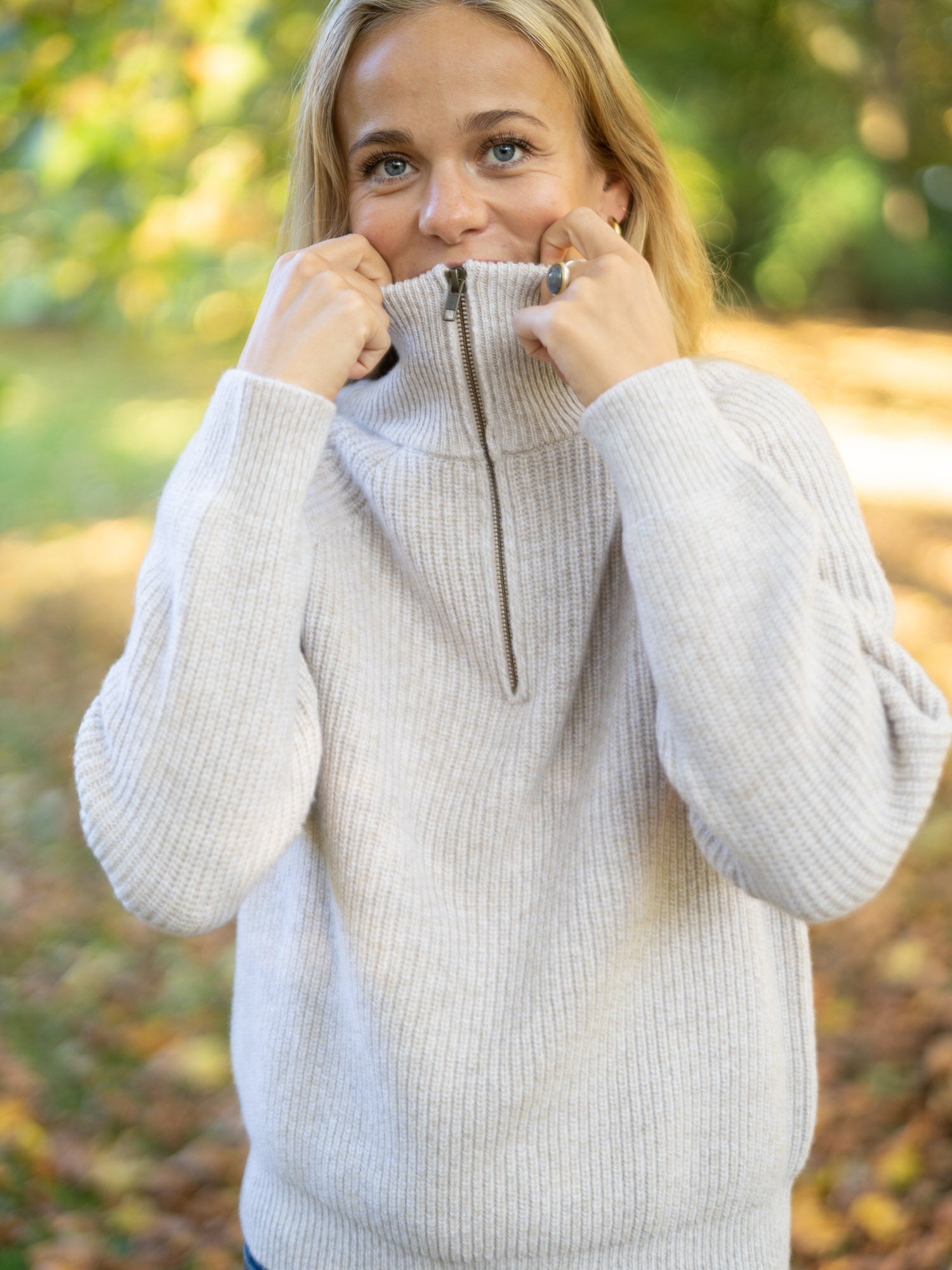 Eine junge, blonde Frau trägt einen nachhaltig und fair produzierten Fari Fashion Troyer von FUXBAU aus 100% Merinowolle in der Natur im Herbst.