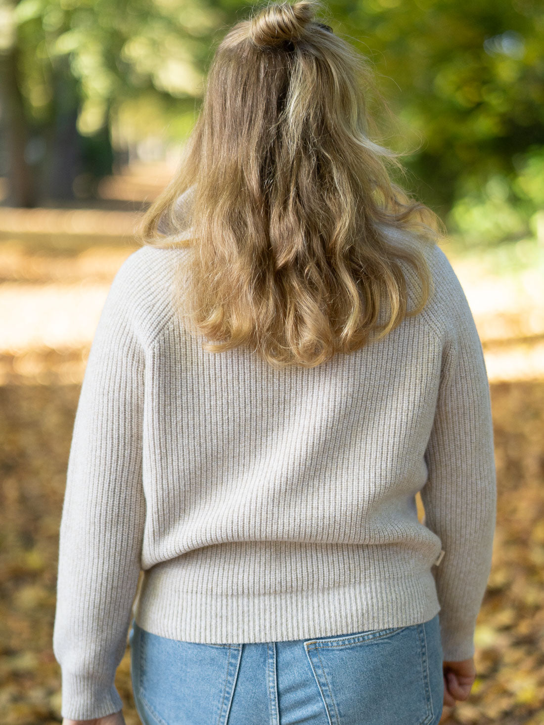 Eine junge, blonde Frau trägt einen nachhaltig und fair produzierten Fari Fashion Troyer von FUXBAU aus 100% Merinowolle in der Natur im Herbst.