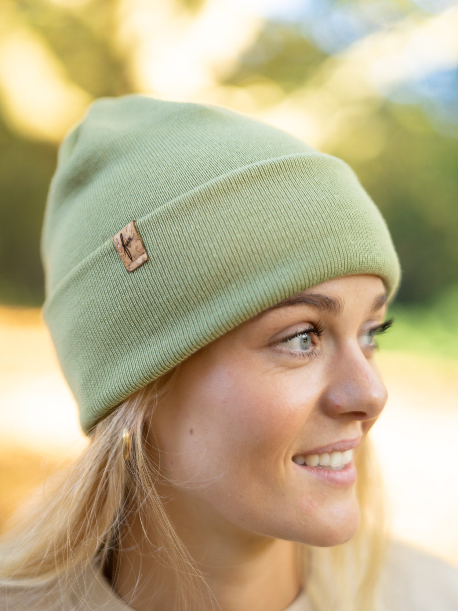 Limitierte und nachhaltige Fair Fashion FUXBAU Merino Kork Beanie in Der Farbe Pistazie. Getragen von einer jungen, blonden Frau im Herbst. Gefertigt in Deutschland aus 100% Merino Schurwolle.