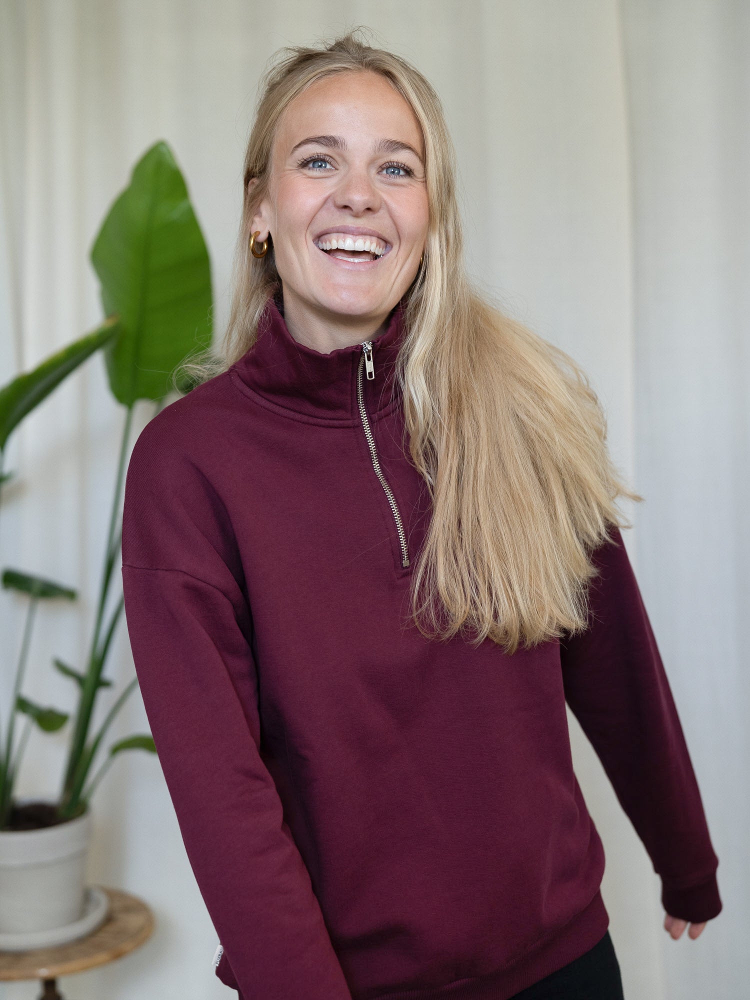 Frau trägt den bordeauxfarbenen FUXBAU Half-Zip Sweater – Fair Fashion Pullover aus Biobaumwolle, hergestellt in Portugal.
