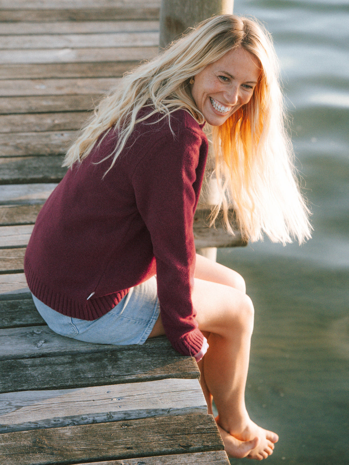 Frauen Merino Strickpullover in Bordeaux aus mulesingfreier Merinowolle beim Sitzen am Wasser