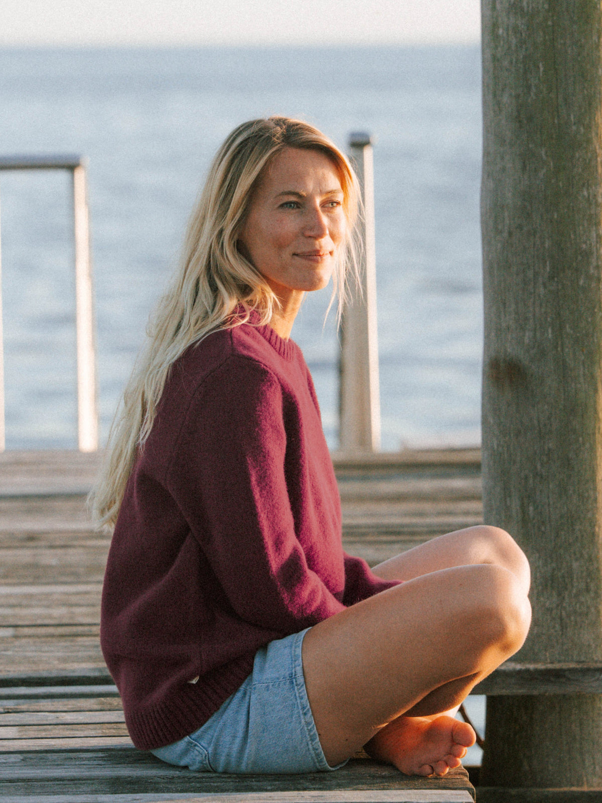 Bordeauxfarbener Merino Strickpullover für Frauen getragen auf einem Holzsteg am Meer