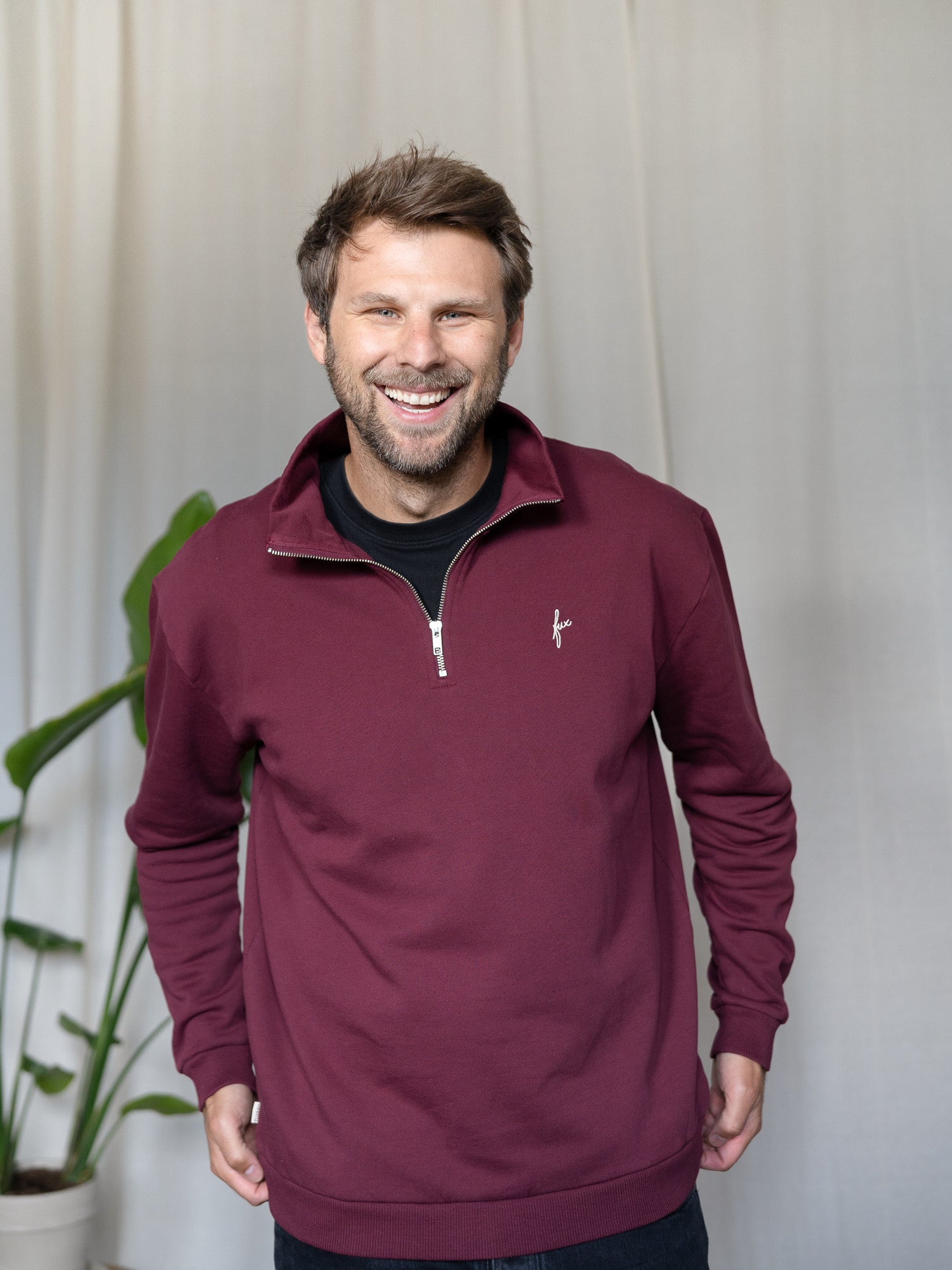 Mann trägt den bordeauxfarbenen FUXBAU Half-Zip Sweater – Fair Fashion Pullover aus Biobaumwolle, nachhaltig hergestellt in Portugal.